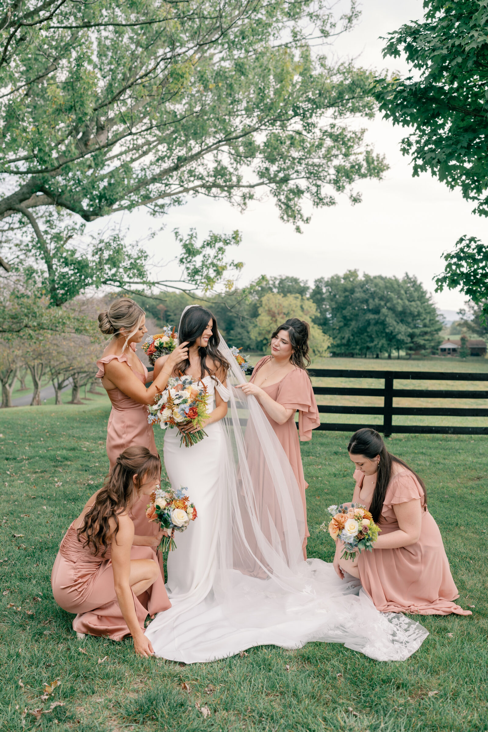 Bride surrounded by bridesmaids in blush dresses adjusting her veil and holding bouquets at Red August Farm wedding in Waynesboro VA