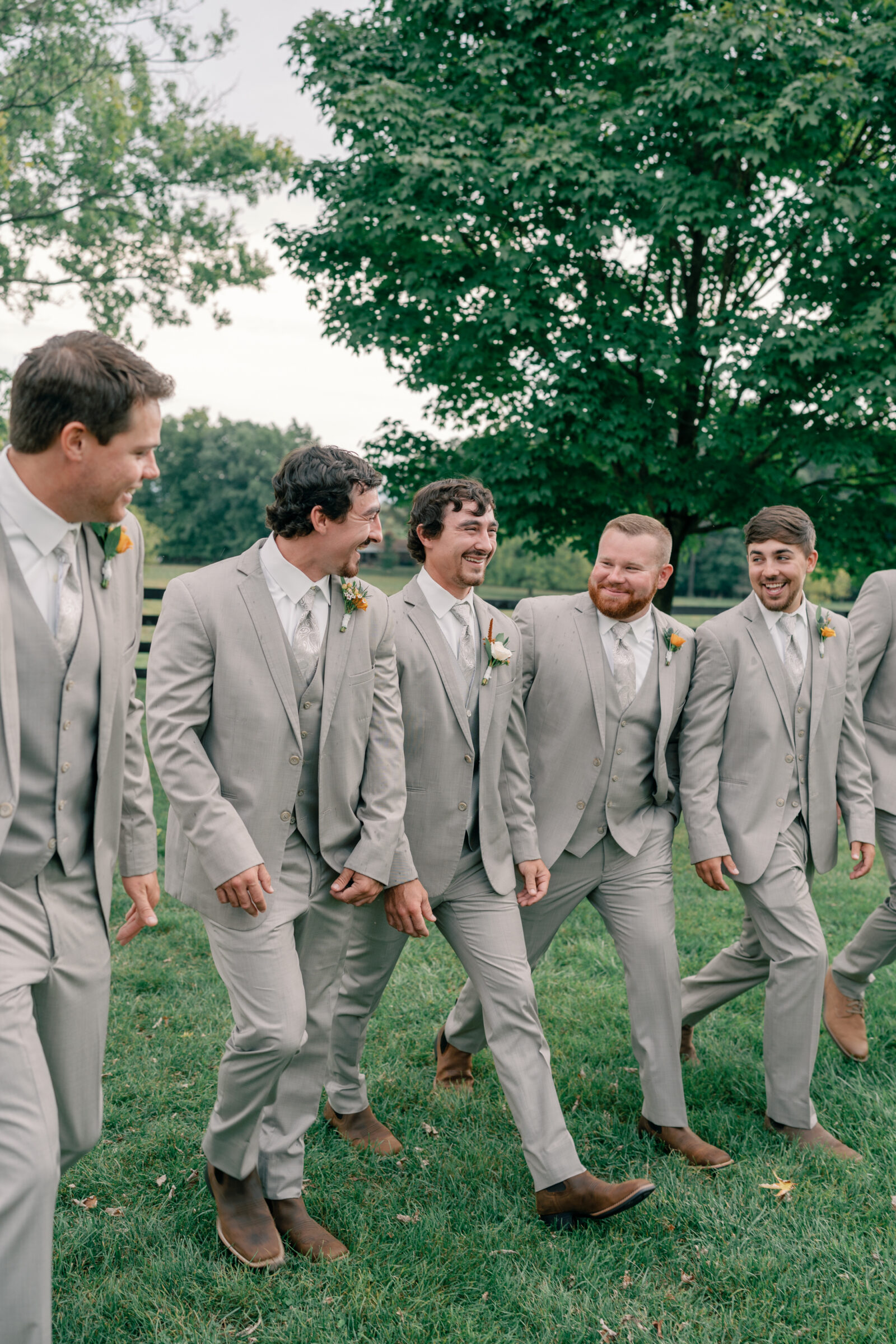 Groom walking with groomsmen in light gray suits and brown boots at Red August Farm wedding in Waynesboro VA