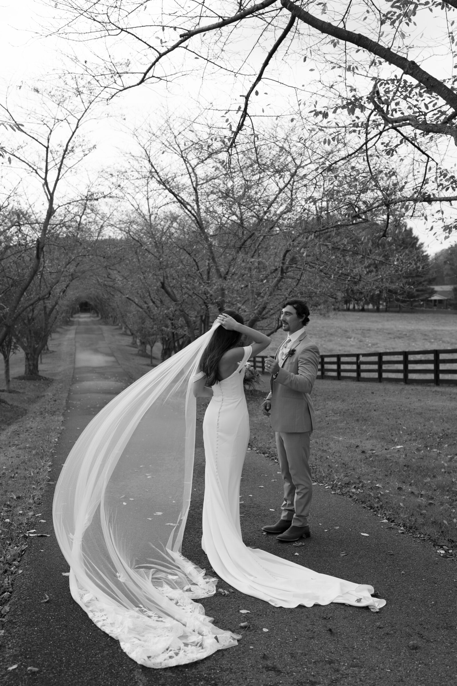 Bride with flowing veil and groom sharing a quiet moment under tree-lined path at Red August Farm wedding in Waynesboro VA