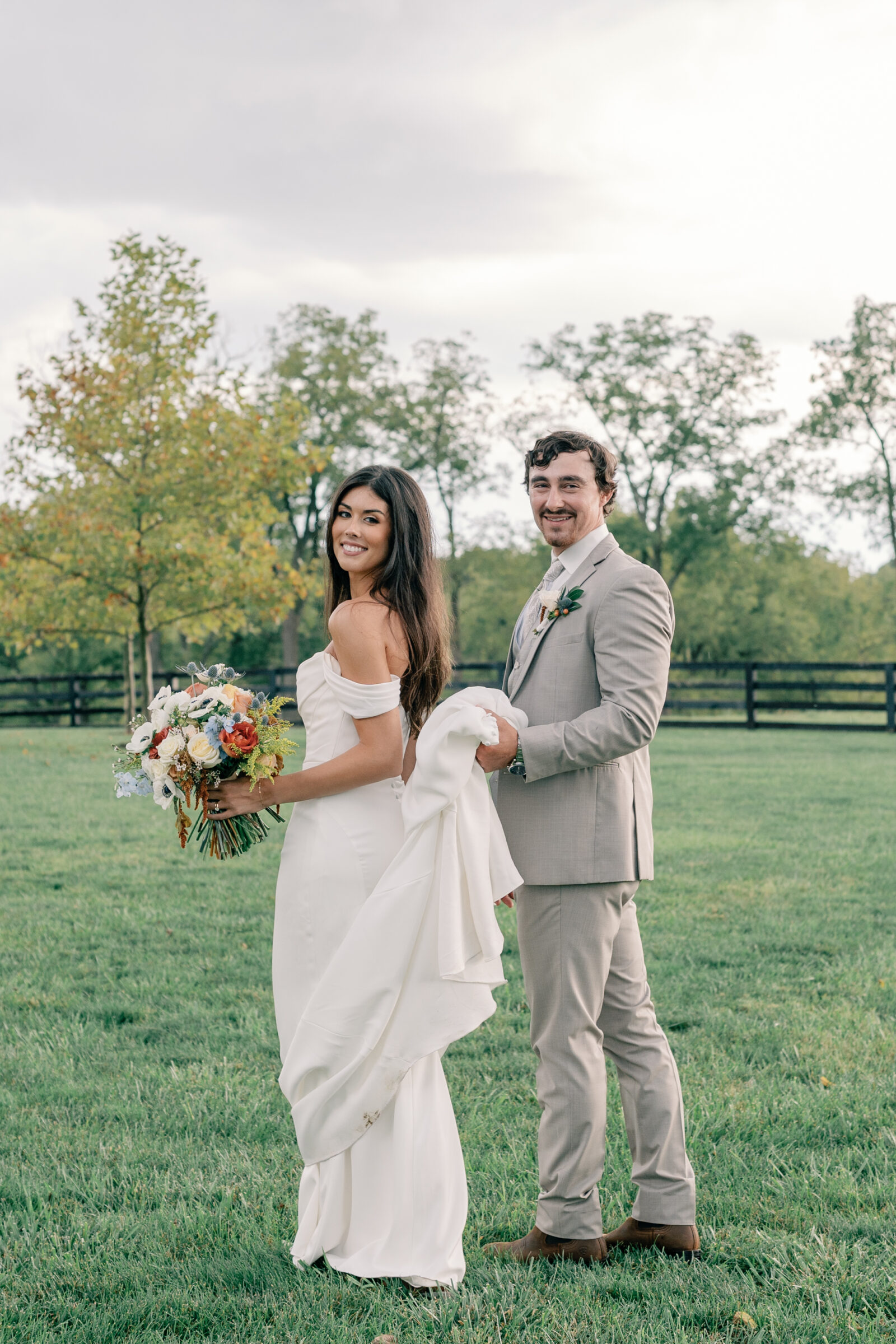 Bride holding colorful bouquet and groom carrying her dress during outdoor portraits at Red August Farm wedding in Waynesboro VA