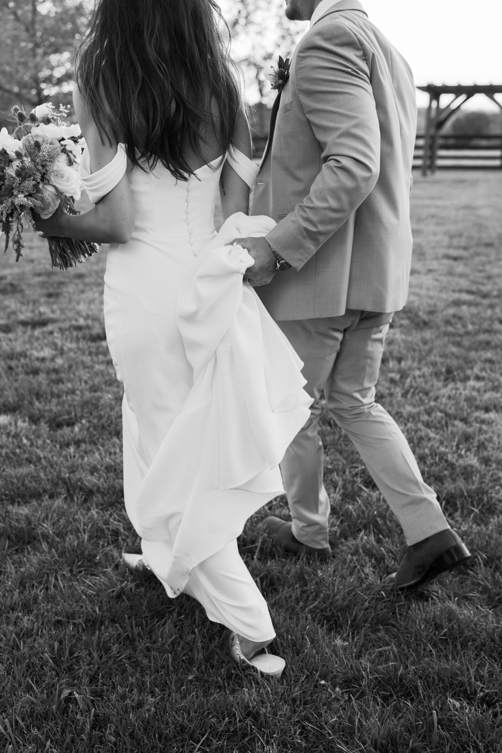 Close-up of bride holding bouquet while groom carries her dress train
