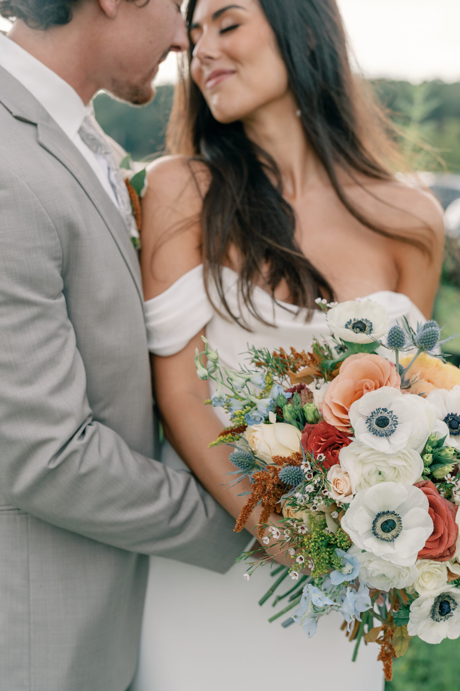 Close-up of bride and groom embracing with colorful bouquet of roses and anemones at a wedding in Virginia