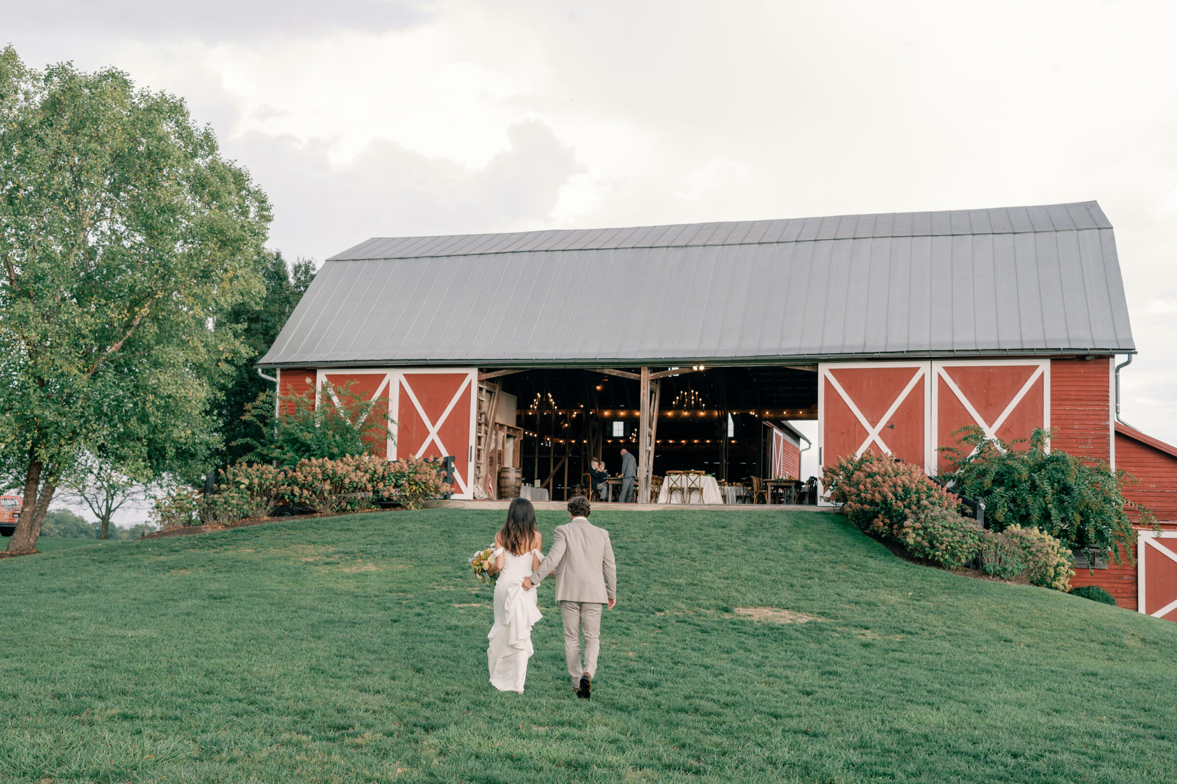 Bride and groom walking toward red barn reception space at Red August Farm wedding in Waynesboro VA