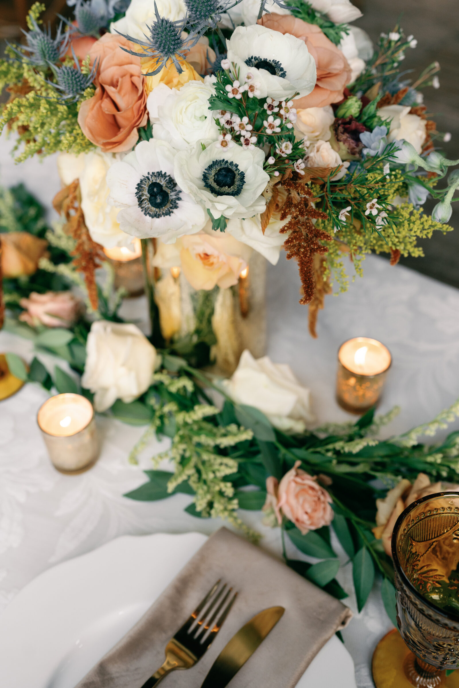 Wedding reception table with floral centerpiece, candles, and gold flatware