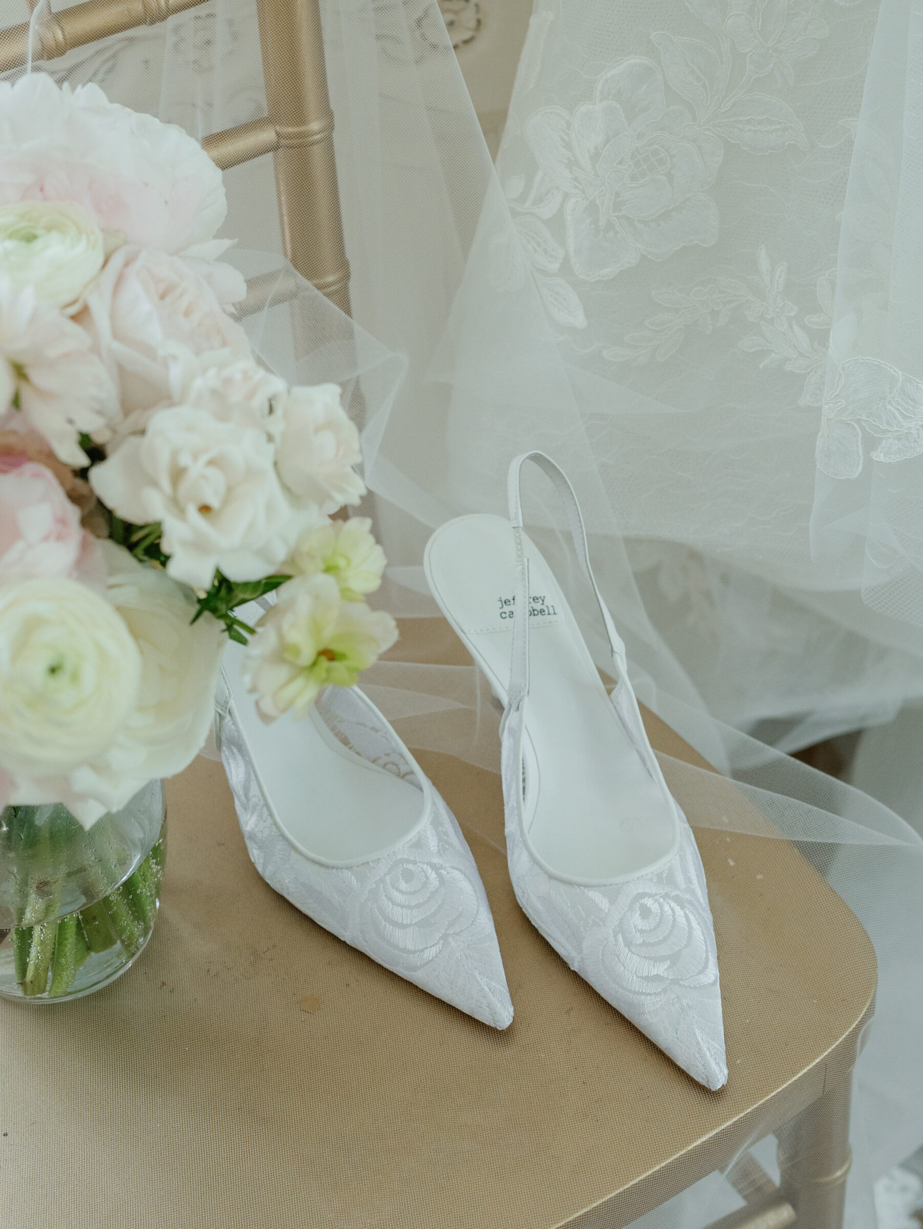 Bridal shoes with floral embroidery styled beside a soft pastel bouquet and the lace of the wedding gown.