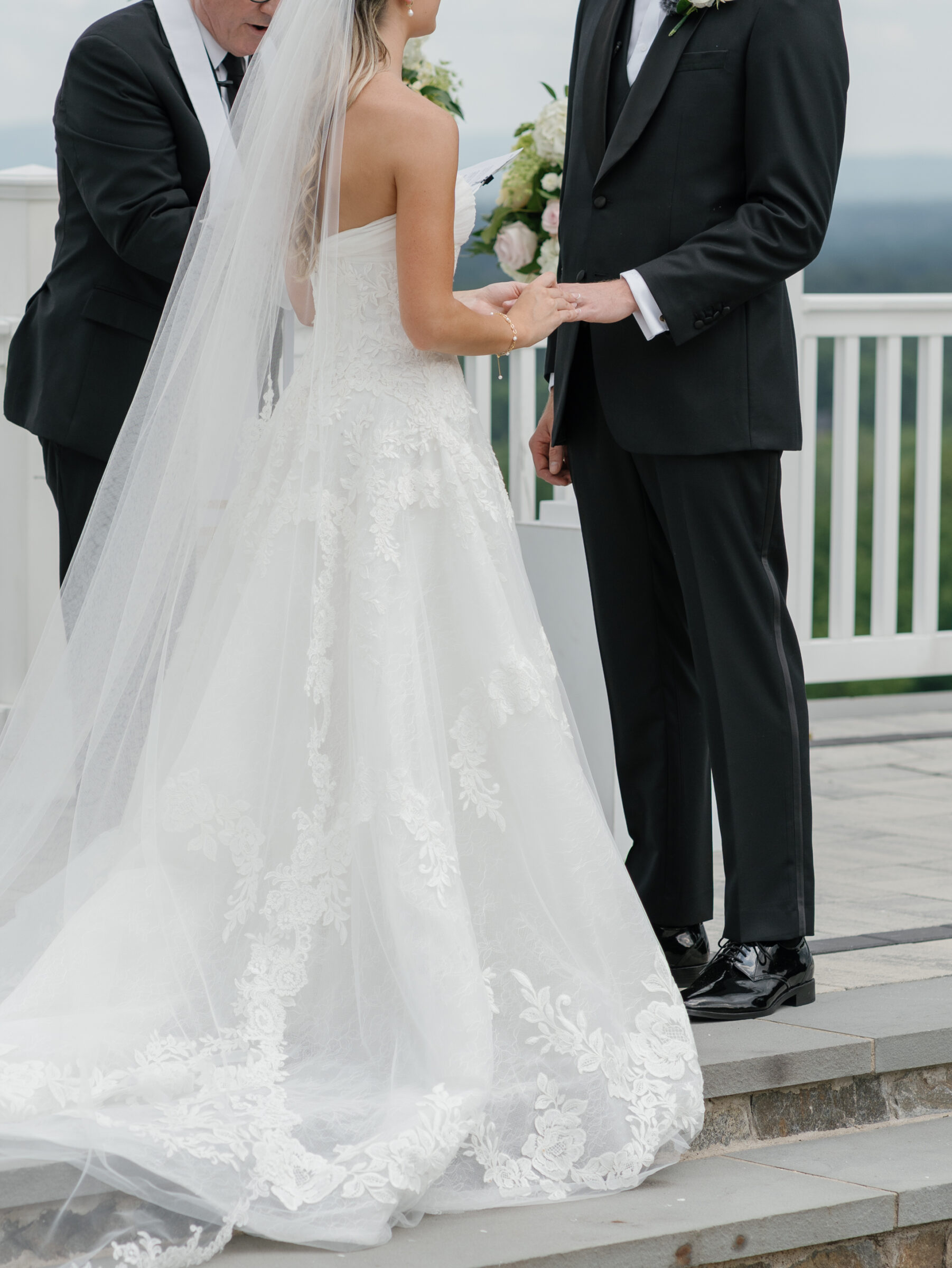 The bride and groom holding hands during the vows at a The View at Bluemont Wedding, with her lace gown flowing over the terrace steps.