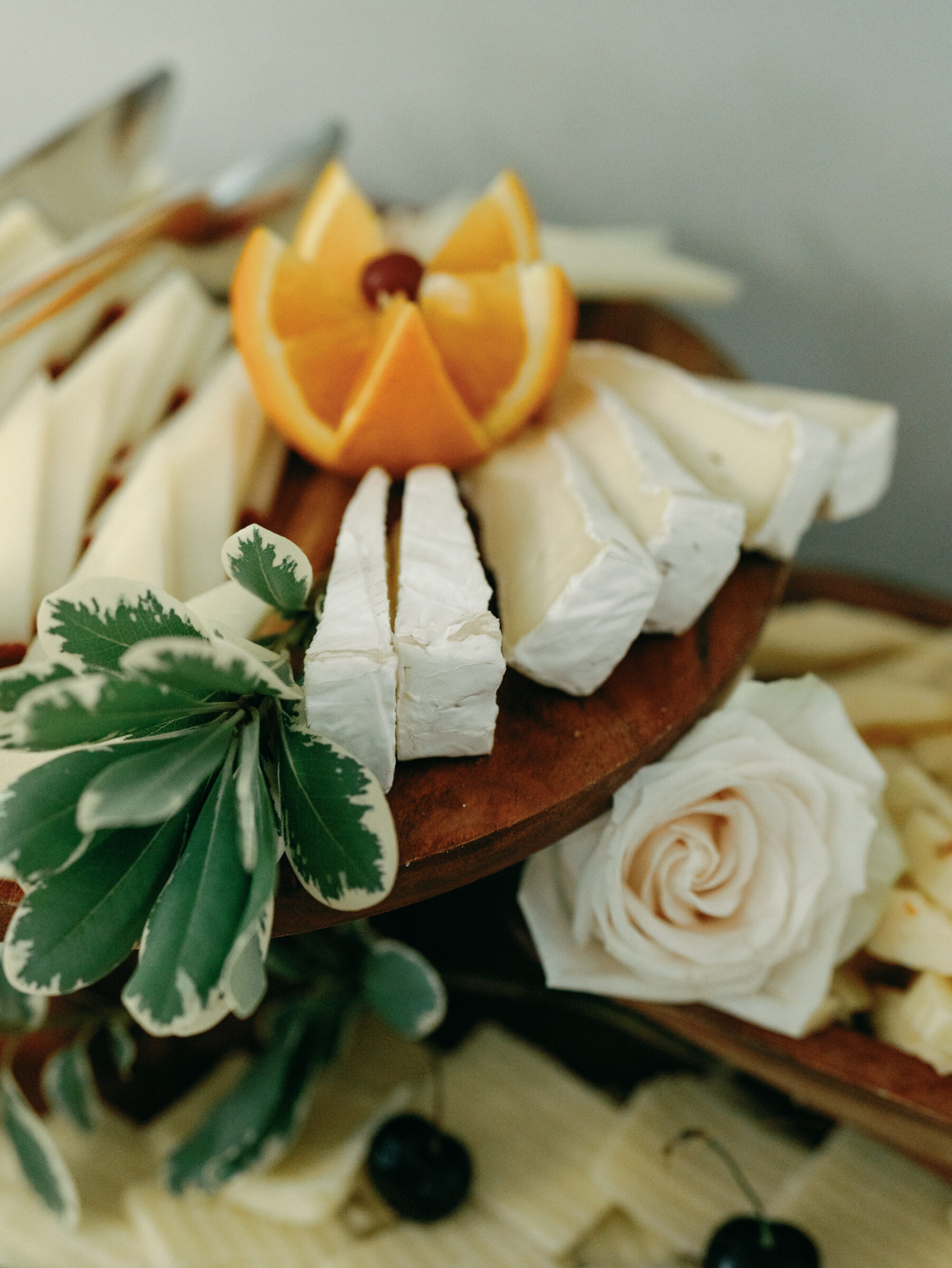 Artfully styled cheese board featuring creamy brie, citrus, greenery, and a single rose for a sophisticated wedding reception detail.