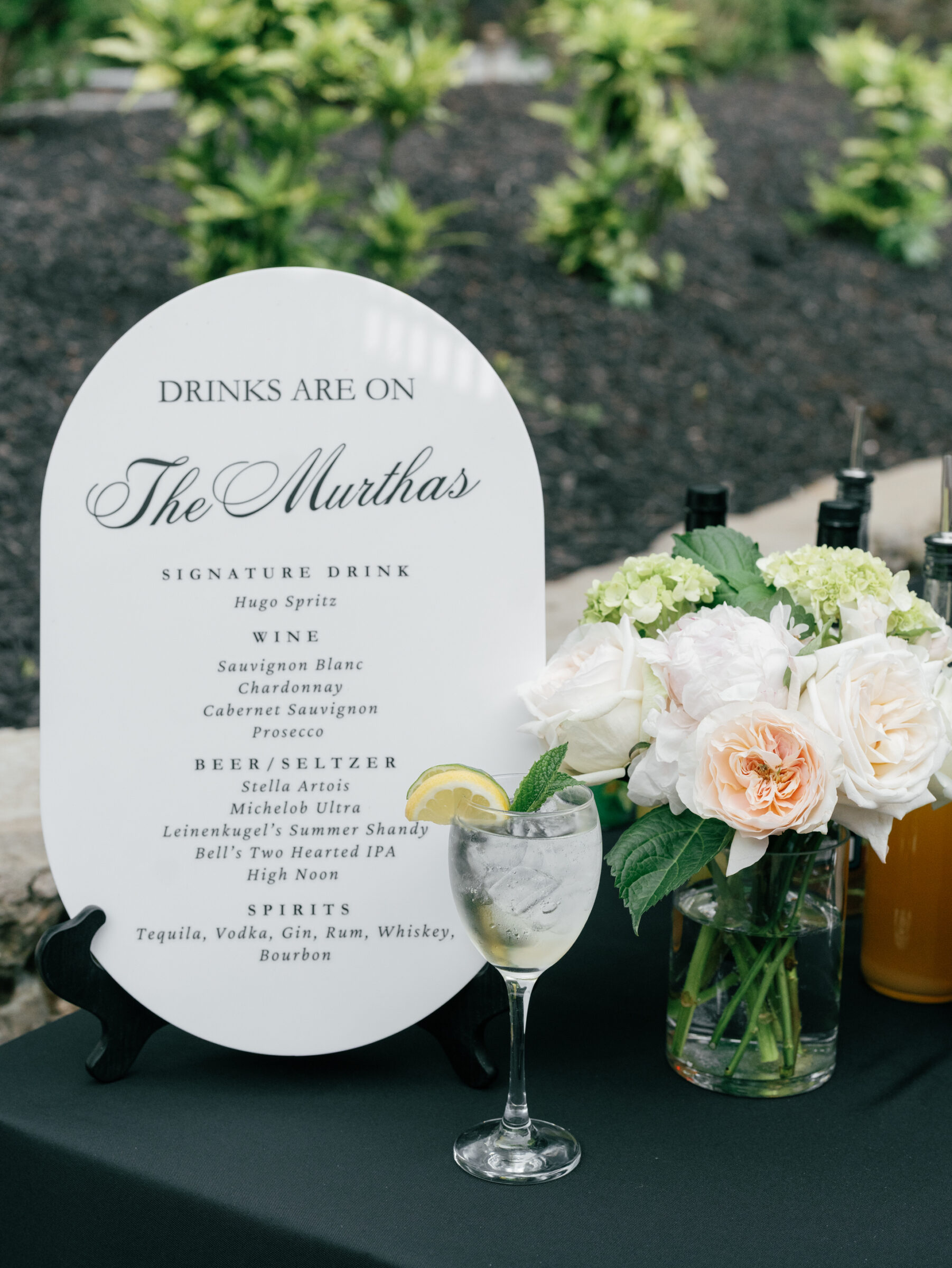 Elegant cocktail display with personalized drink signage, a fresh summer spritz, and romantic florals at the bar.