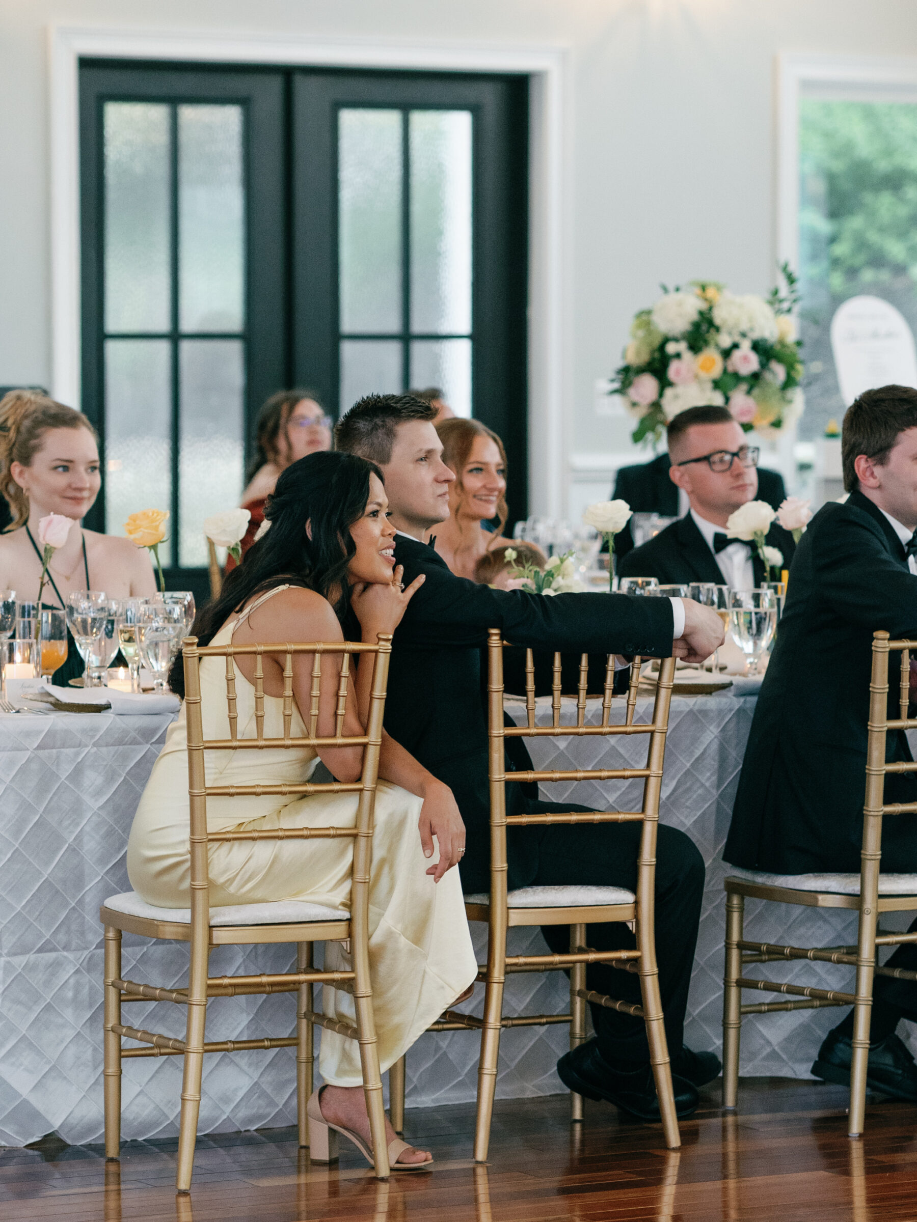 Wedding guests seated together, watching the reception events with smiles and soft candlelight around them.