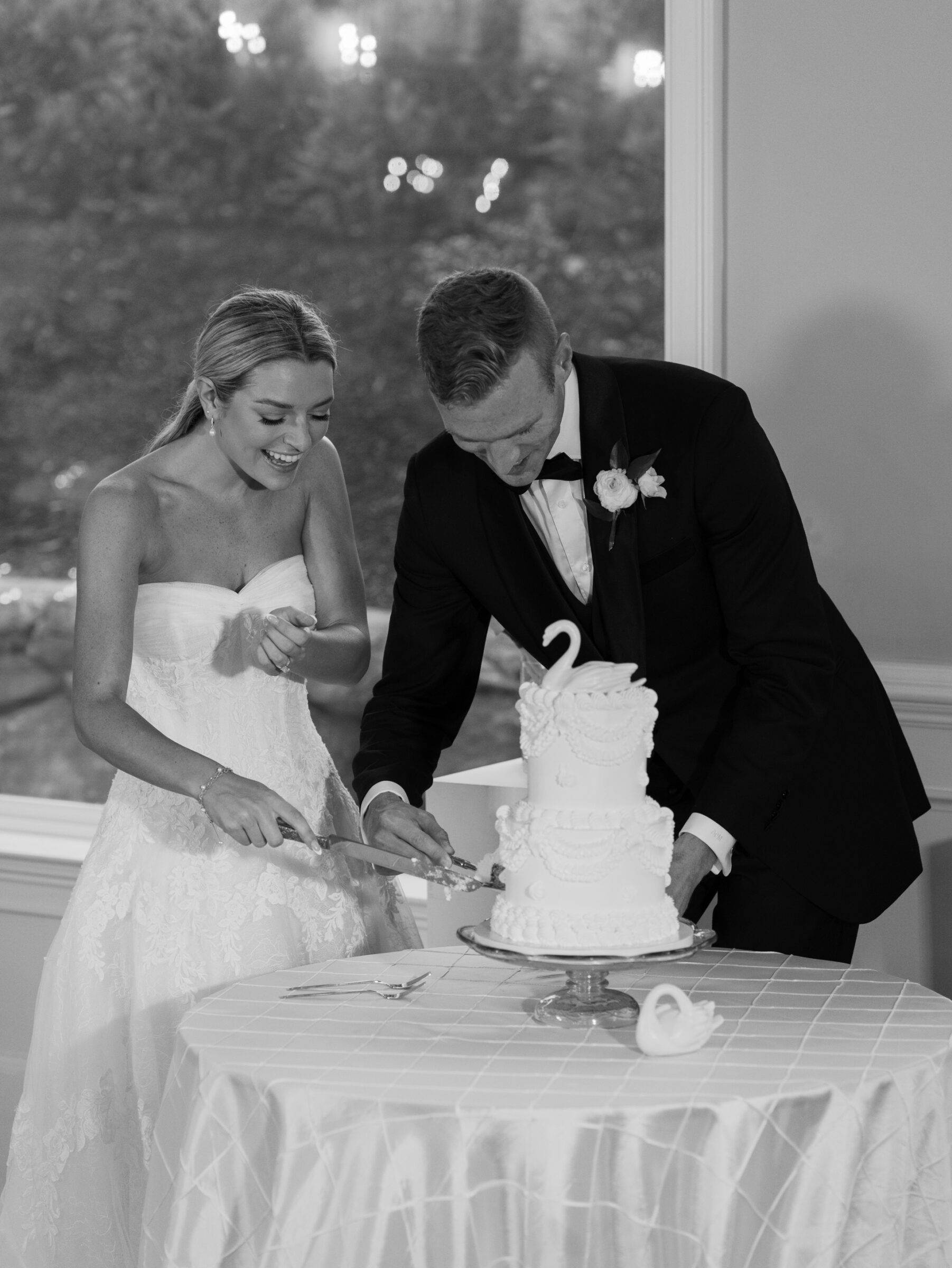 The bride and groom laugh together as they slice into their wedding cake during the reception.