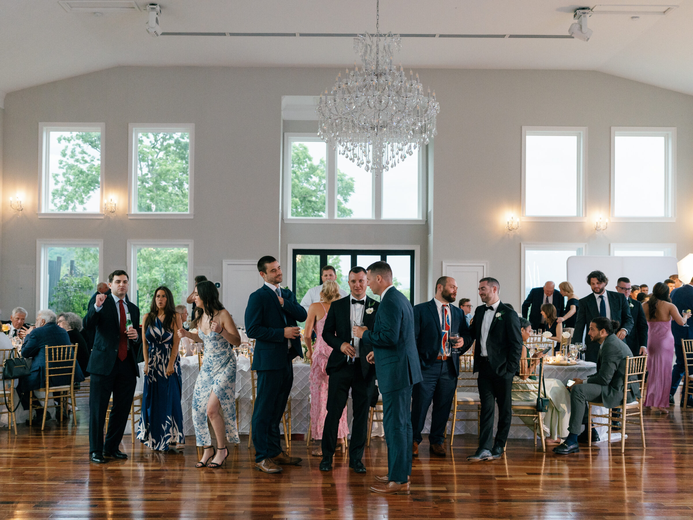 Wedding guests mingle during the reception at The View at Bluemont, surrounded by soft neutral décor and crystal chandeliers.