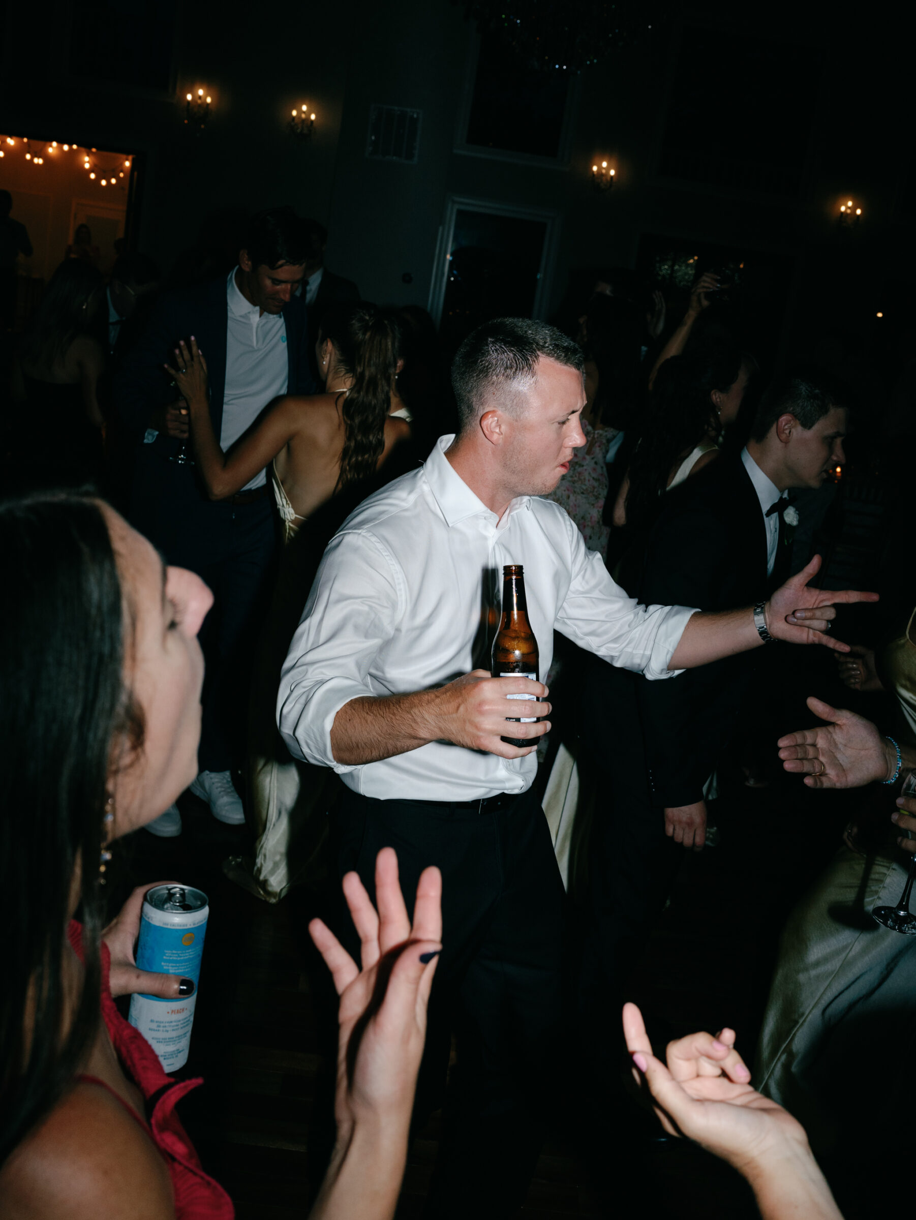 Wedding guests dancing and celebrating on the dance floor with drinks in hand during the reception.