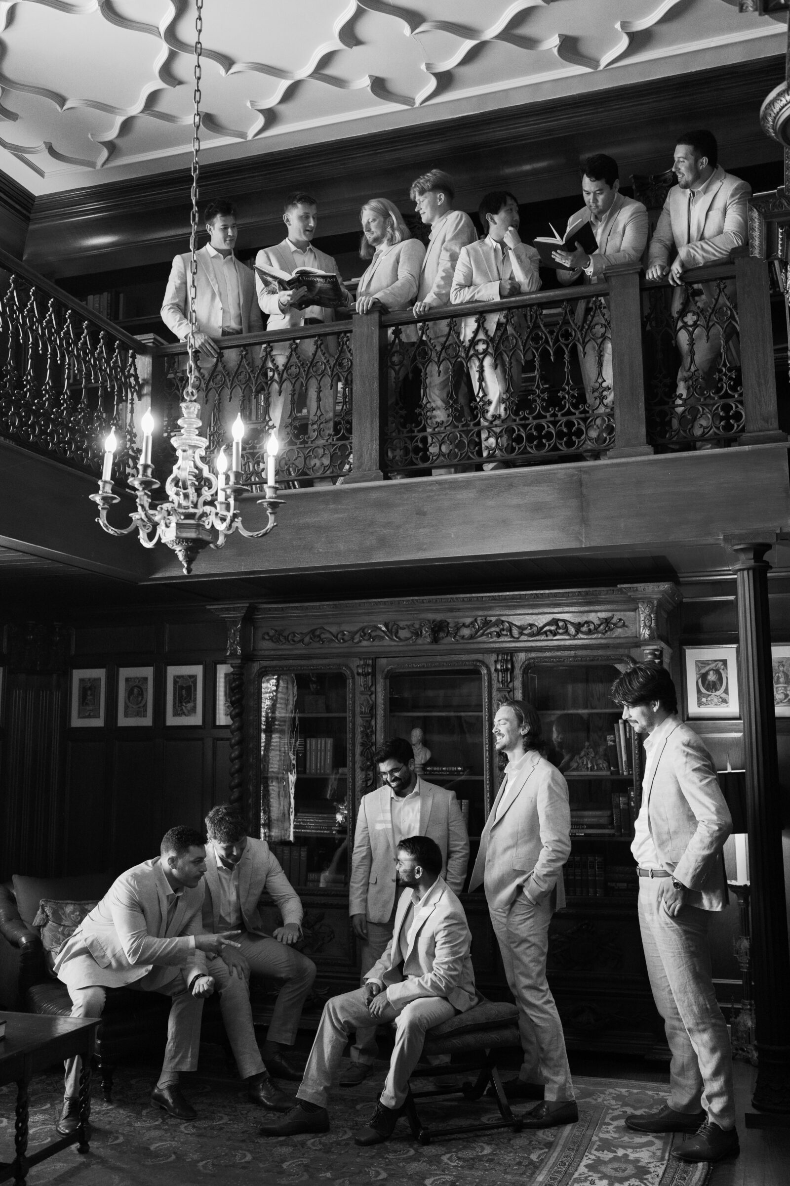 Groomsmen in light suits gather inside Dover Hall’s library, sharing laughter and conversation beneath the grand chandelier — captured by a Richmond wedding photographer.