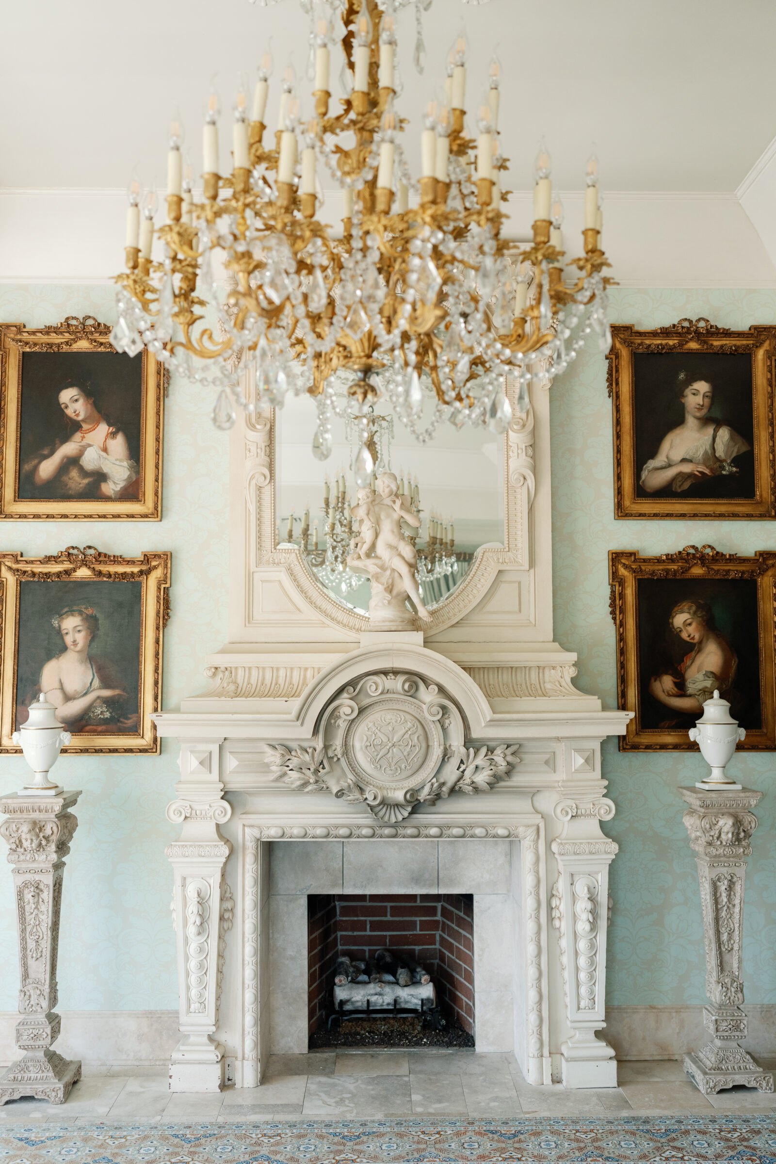 Elegant interior of Dover Hall featuring a grand white fireplace, gold-framed portraits, and a crystal chandelier.