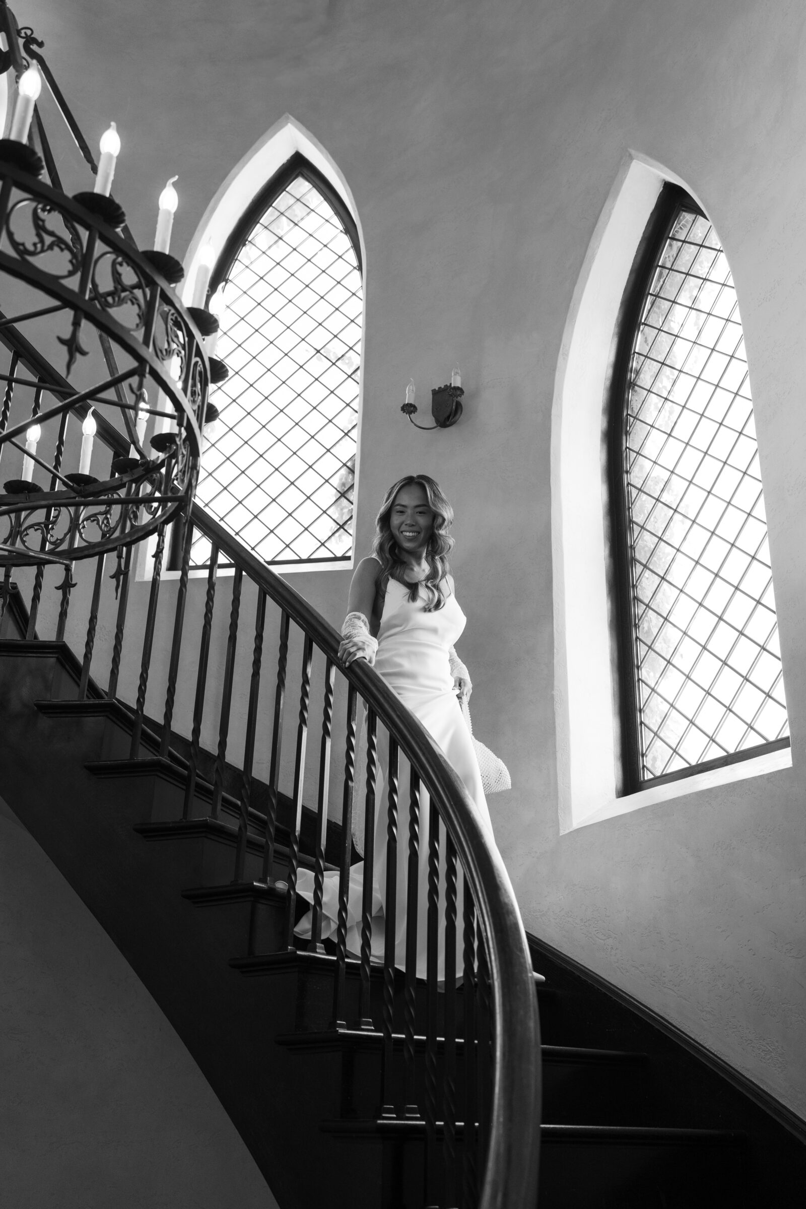 Bride descending the grand staircase at Dover Hall, framed by arched windows and soft natural light — a timeless black and white moment captured by a Richmond wedding photographer during a Dover Hall wedding.
