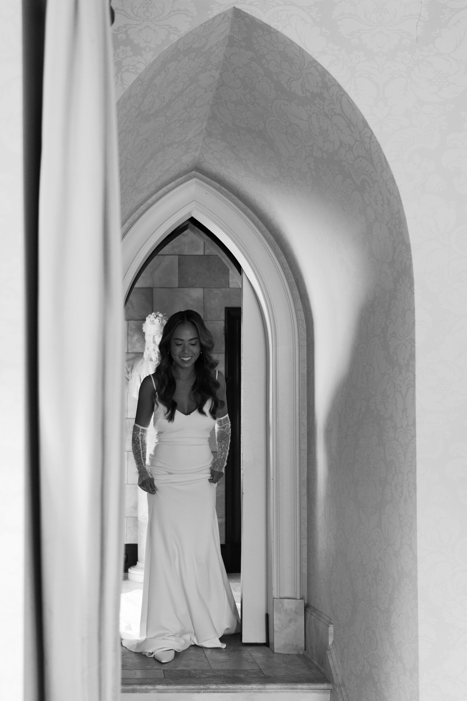 Bride walking through an arched doorway, wearing a classic fitted gown and lace sleeves — captured by a Richmond wedding photographer.