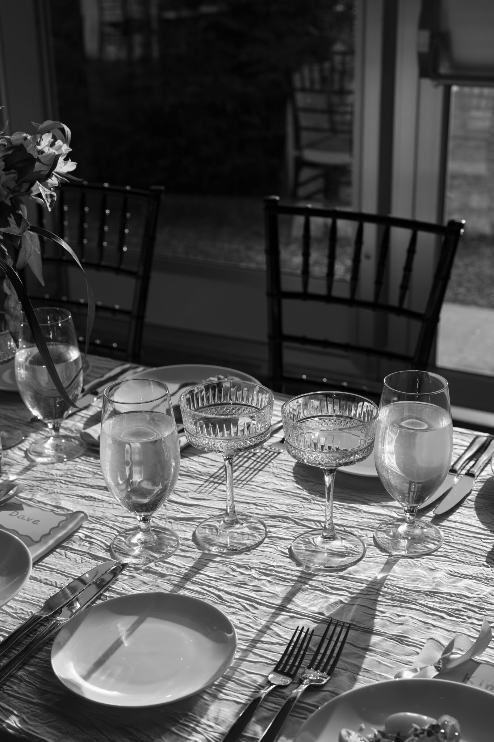 Black and white detail of a reception table at Dover Hall, featuring elegant glassware, soft natural light, and classic black chiavari chairs.