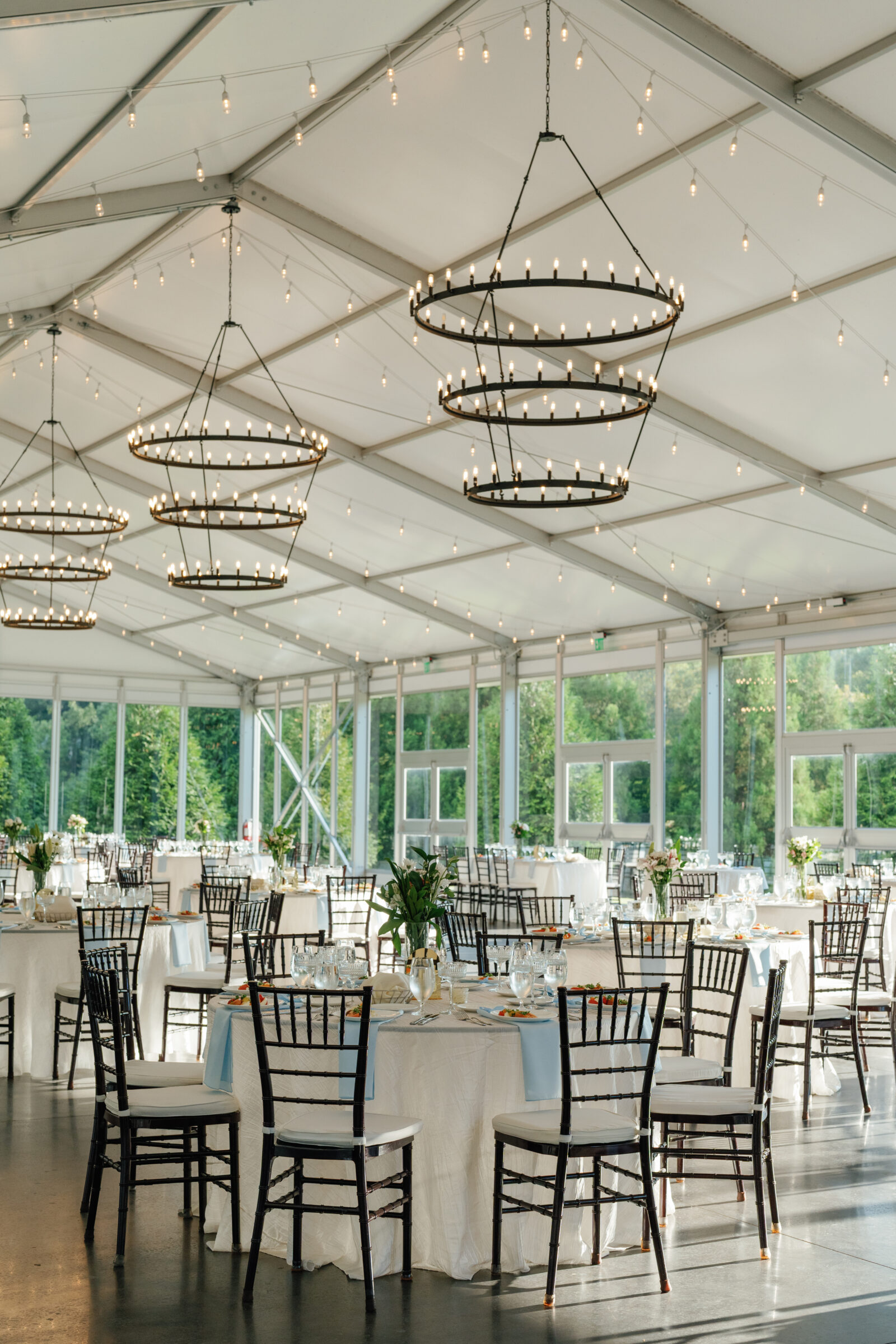 Tented reception space at Dover Hall with round tables, soft pastel linens, and black chiavari chairs beneath glowing chandeliers — elegant summer reception styling captured by a Richmond wedding photographer during a Dover Hall wedding.