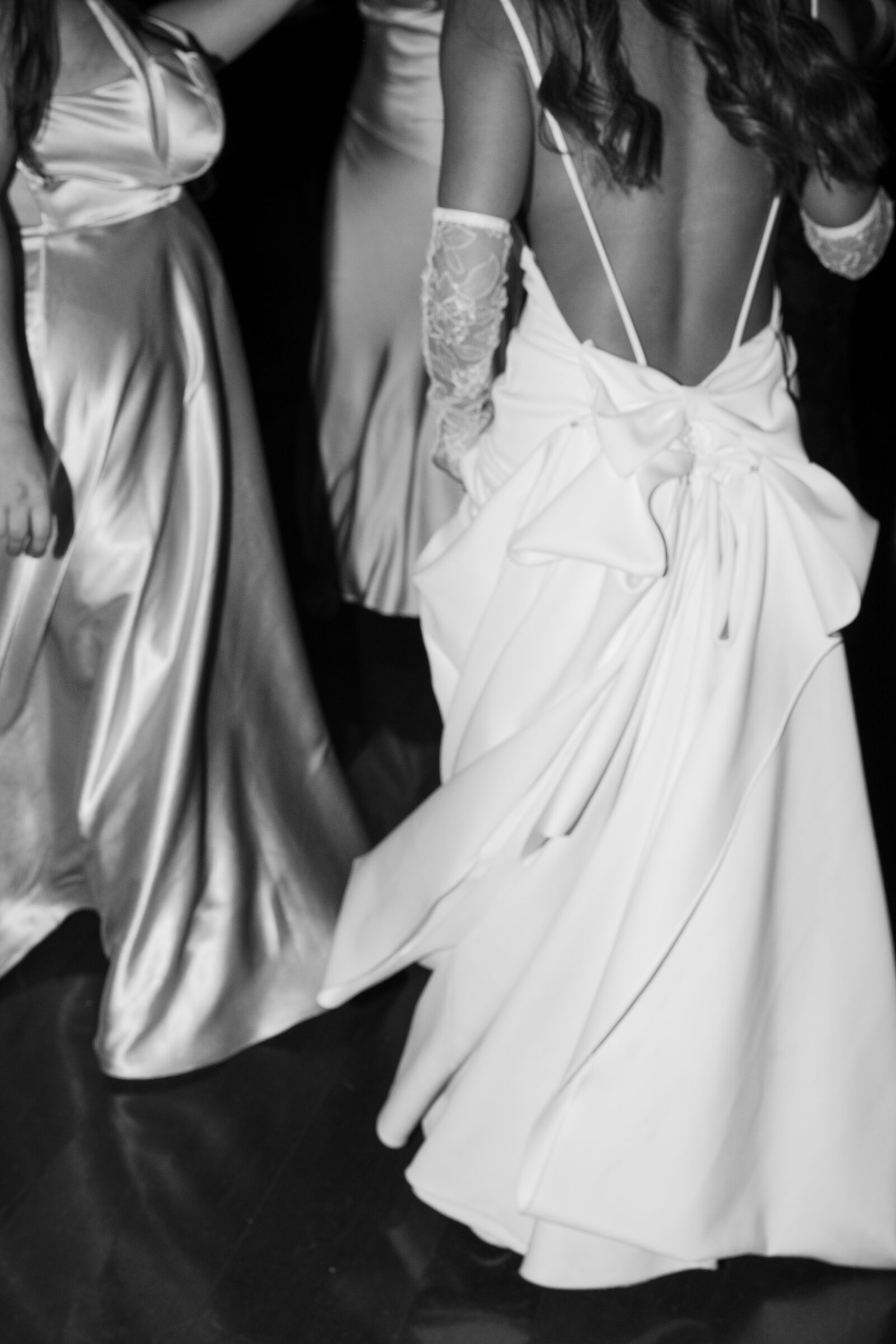 Bride dancing at Dover Hall reception in an elegant gown with a dramatic bow detail, surrounded by guests in satin dresses — a refined yet joyful wedding moment captured by a Richmond wedding photographer.