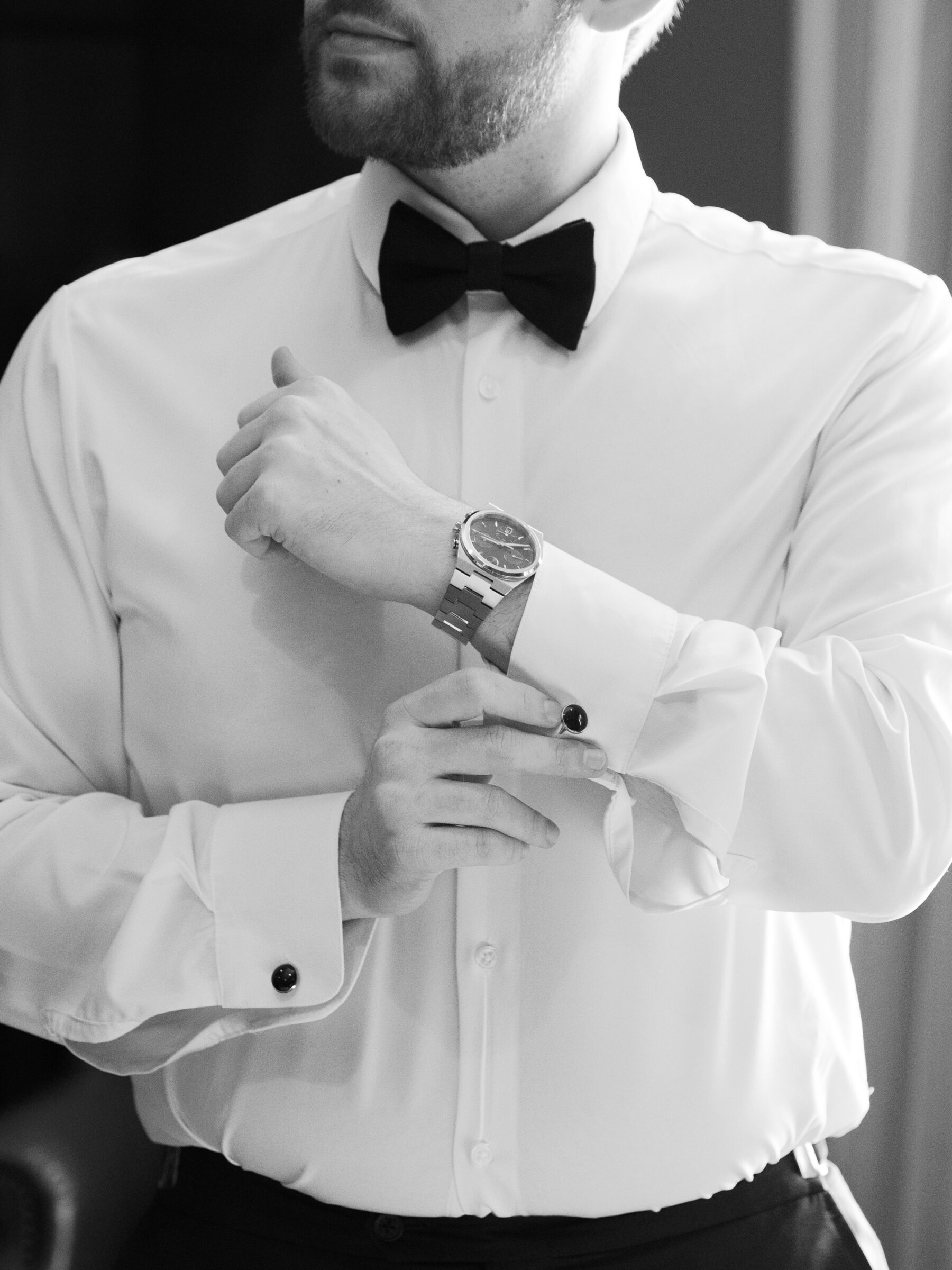 Hermitage Country Club Wedding | Groom adjusting his cufflinks while wearing a classic white dress shirt, black bow tie, and wristwatch before the wedding ceremony.