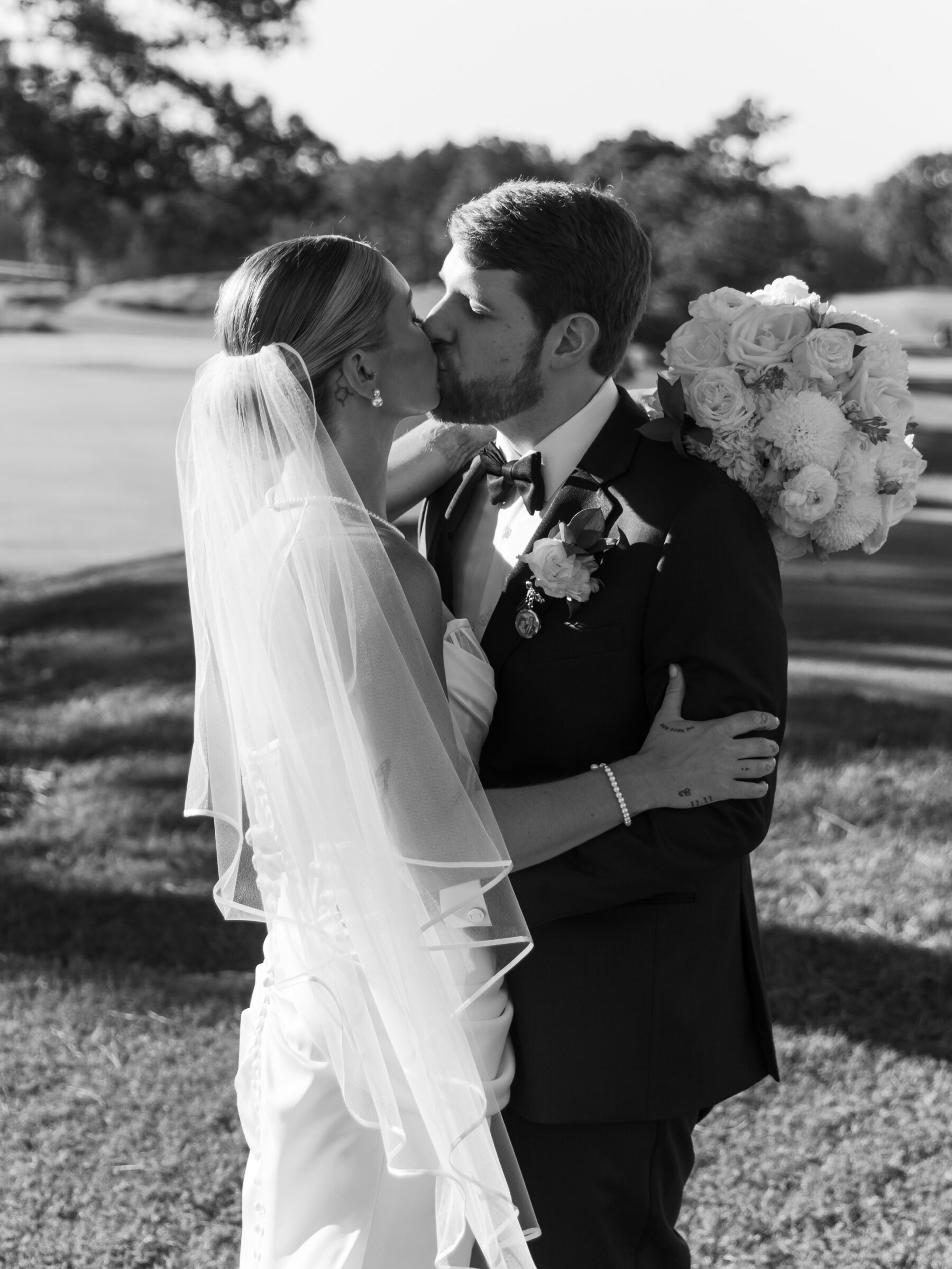 Bride and groom sharing a kiss outdoors after their ceremony, with the bride holding her bouquet.