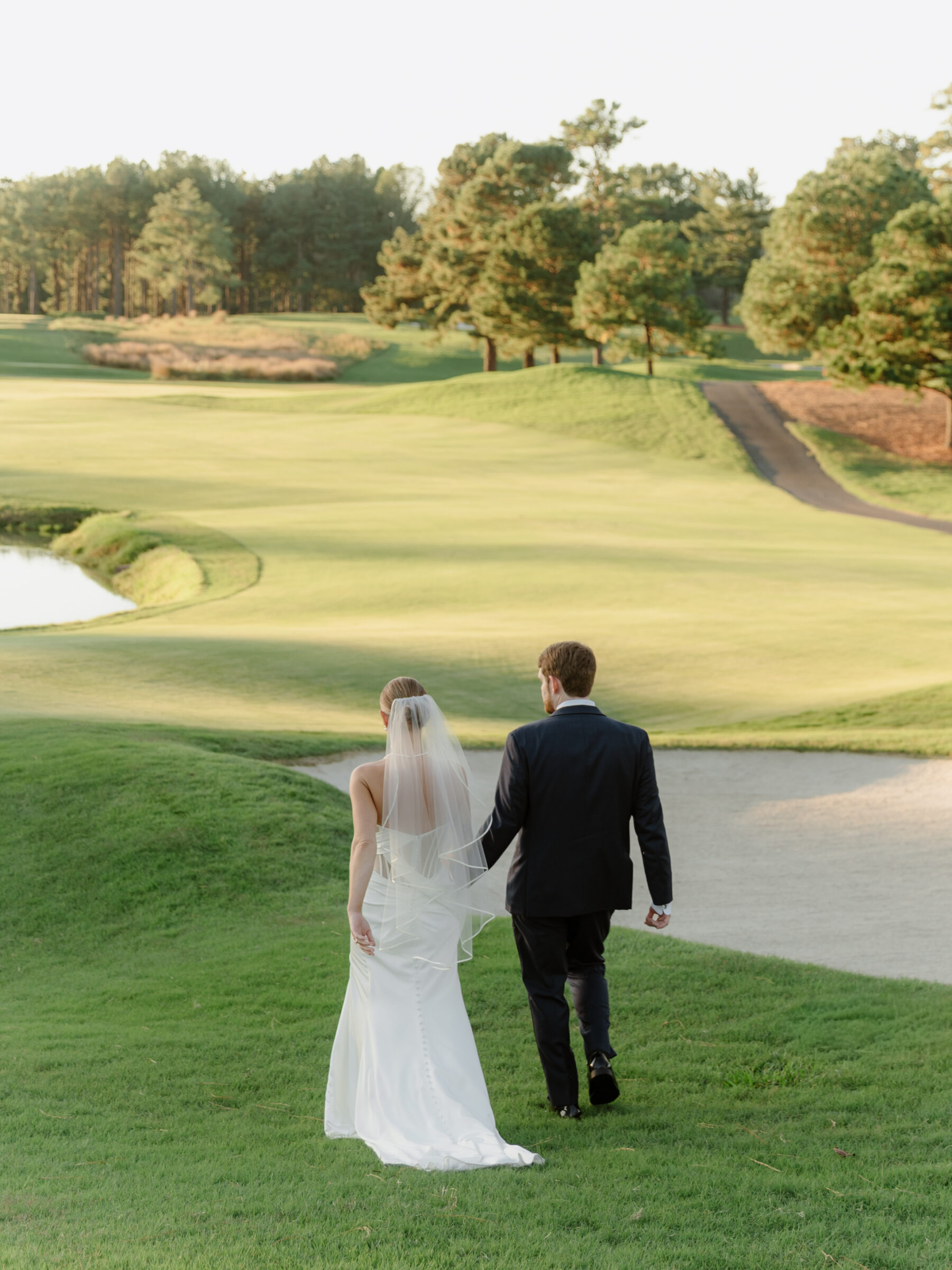 Bride and groom walking together across the golf course during golden hour after their ceremony.