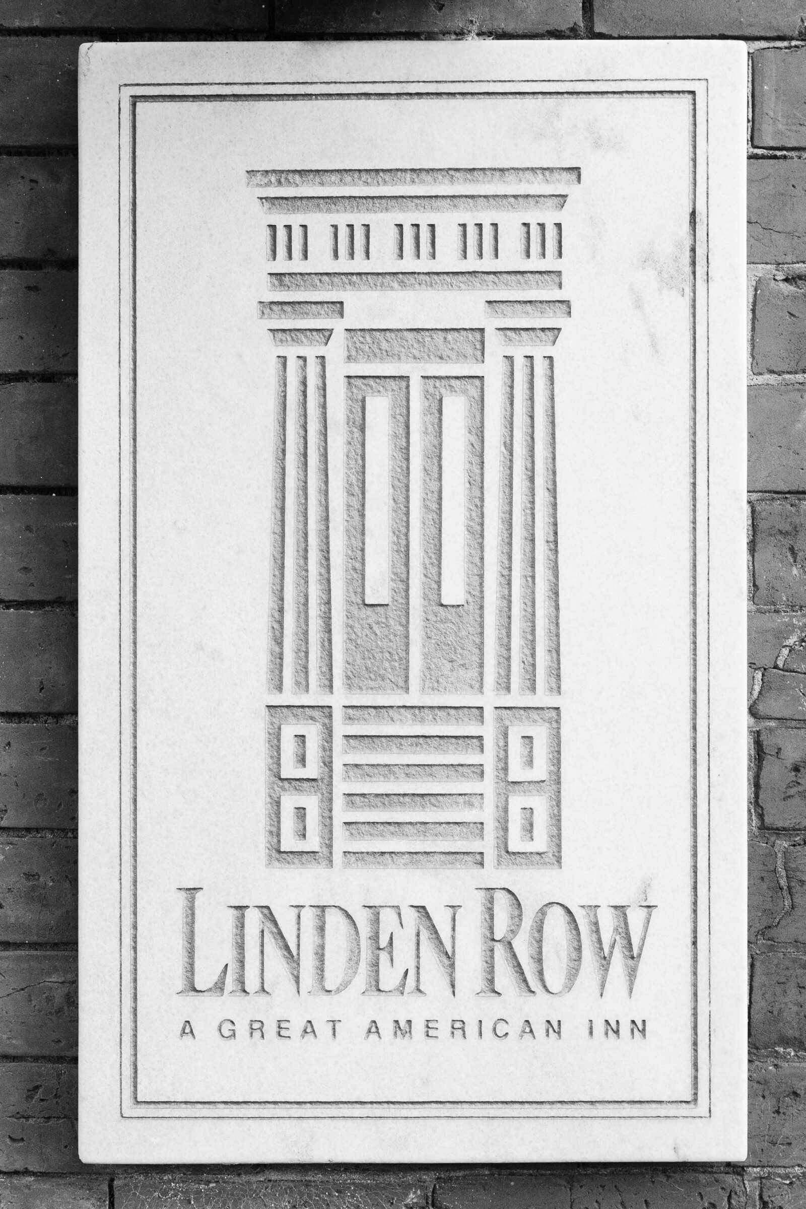 The engraved exterior sign for Linden Row Inn, featuring a carved architectural design and the words “Linden Row, A Great American Inn,” mounted against a brick wall.