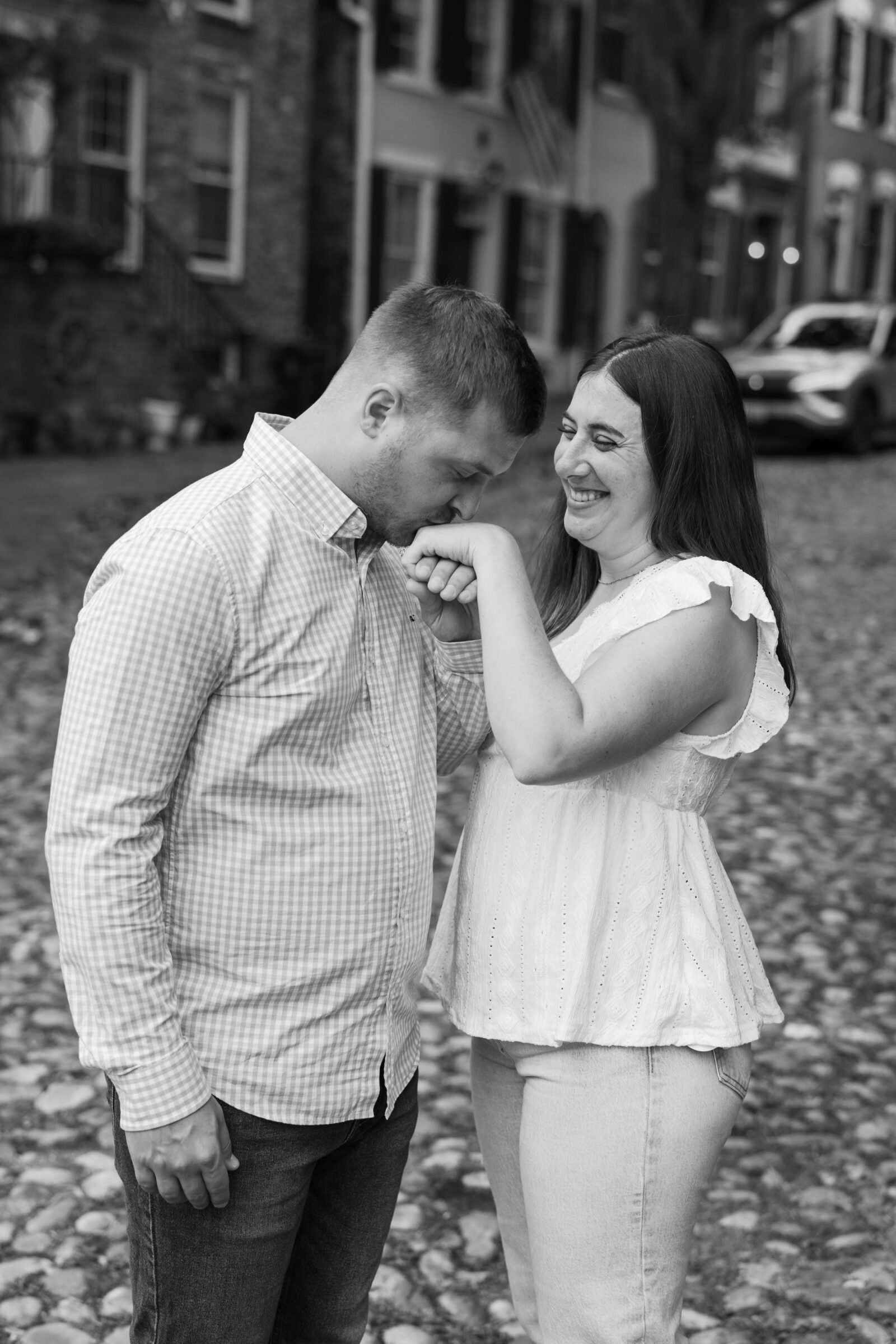 Old Town Alexandria Engagement Photos | Couple sharing a playful moment as he kisses her hand and she smiles on a cobblestone street.