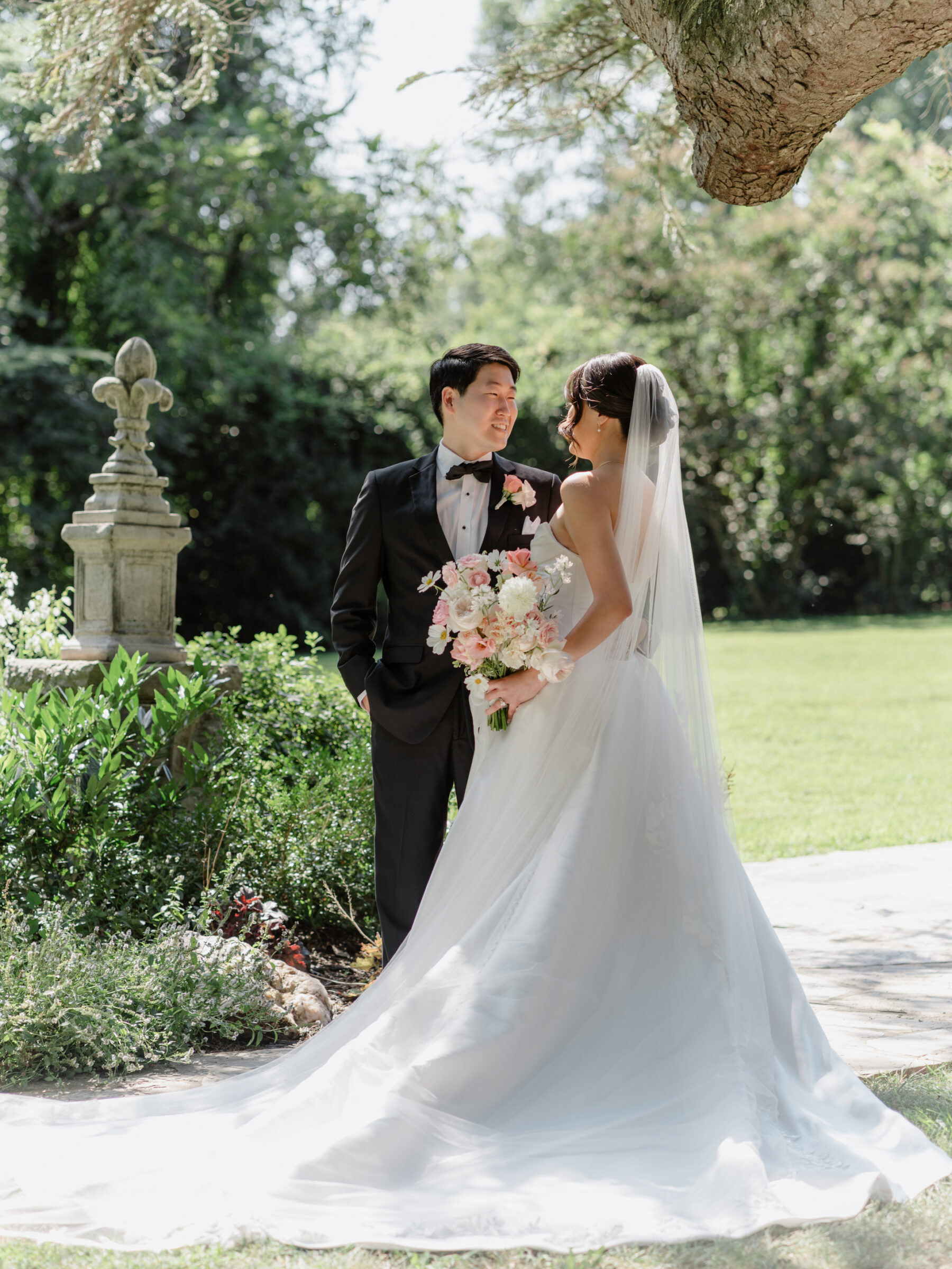 Bride and groom sharing a quiet moment in the garden at Rust Manor House, with the bride’s long train and pink bouquet flowing softly in the summer light.