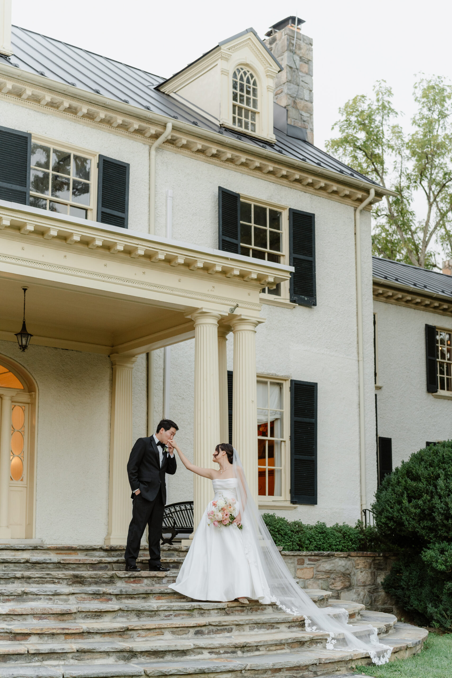 Bride and groom sharing a quiet moment on the stone steps of Rust Manor House, with the bride’s veil trailing behind her and the historic columns framing the scene.