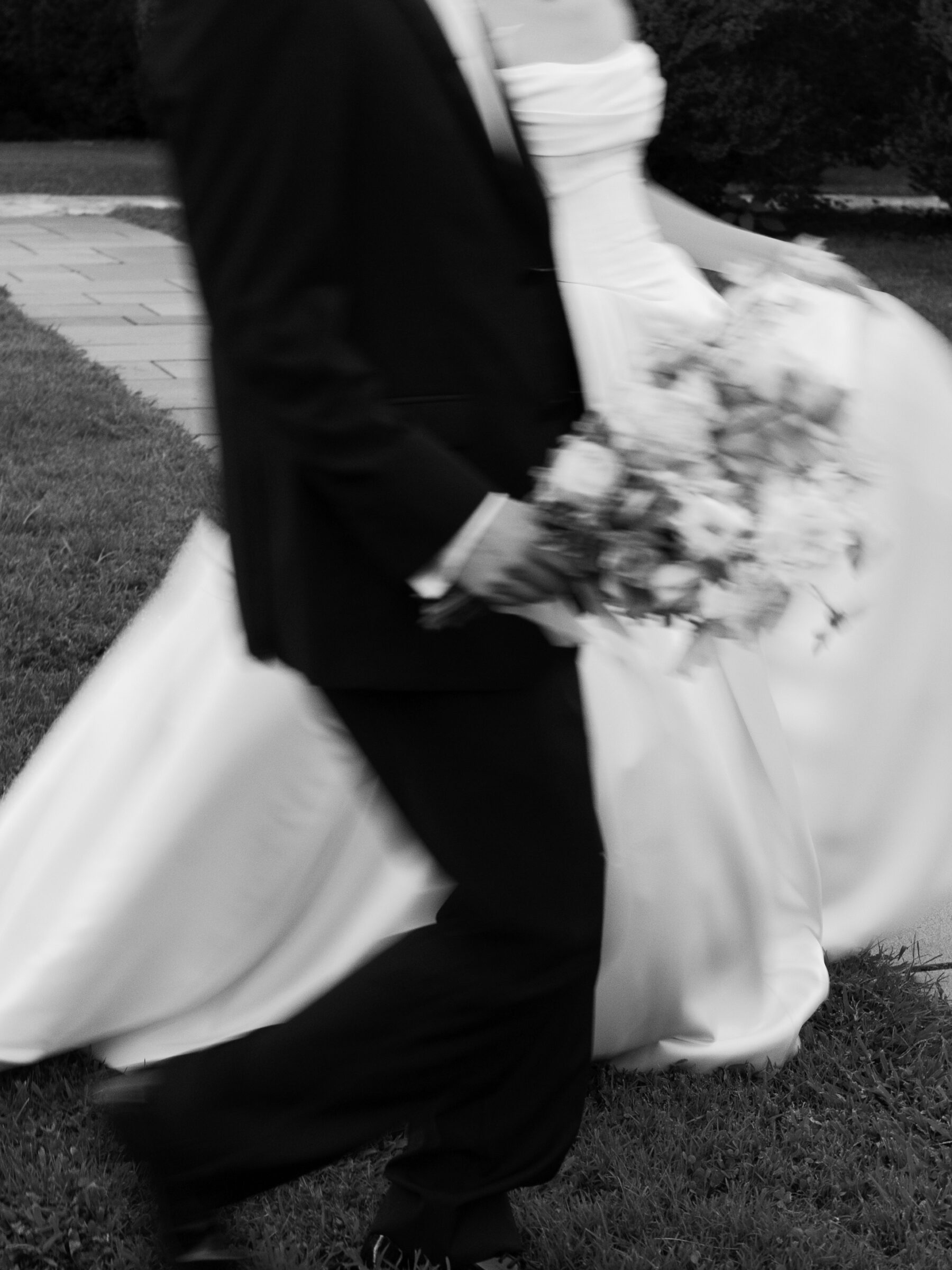 Close-up of the bride’s gown and buttoned back as she walks hand in hand with the groom through the garden.