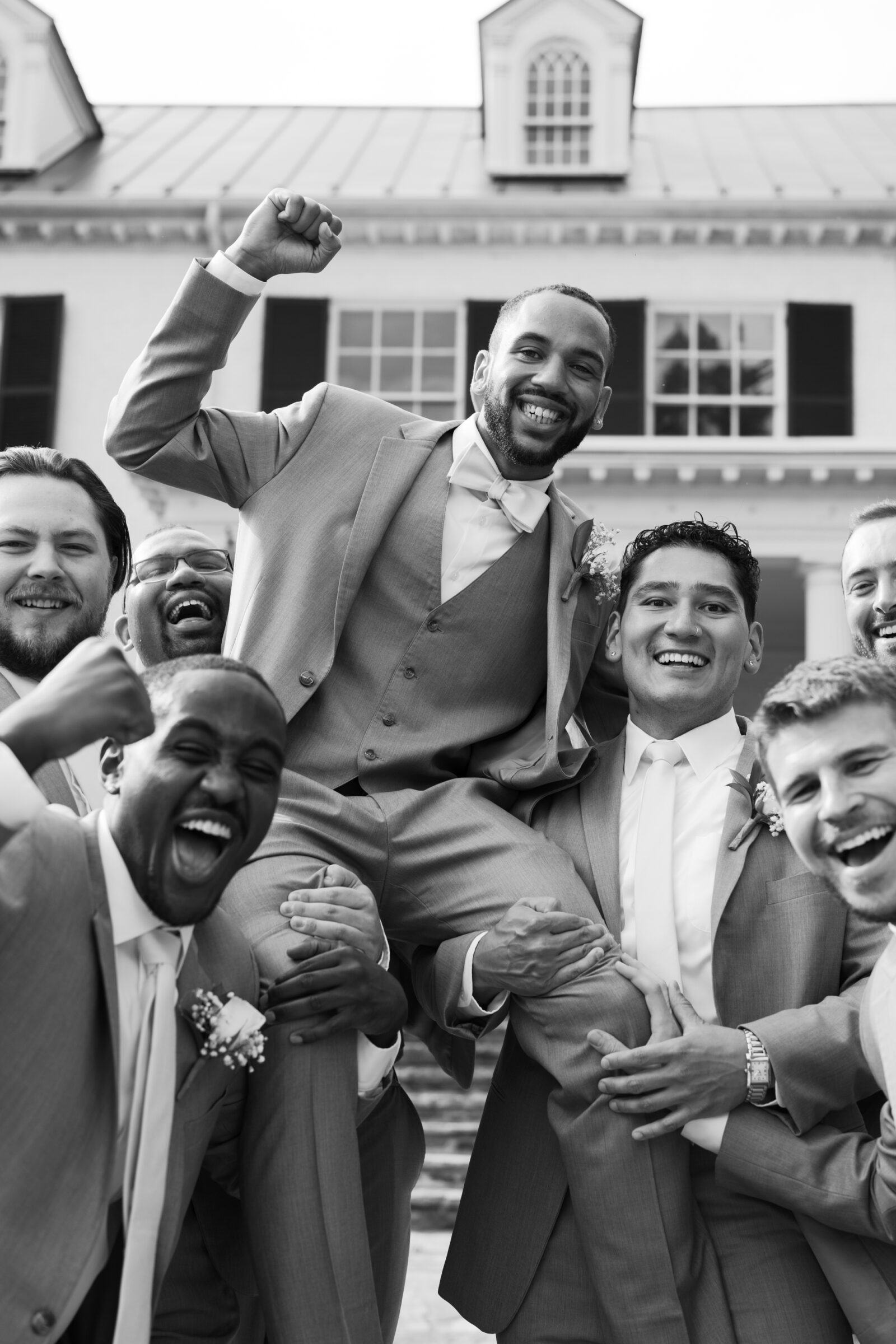 The groom celebrating with his groomsmen as they lift him during portraits.