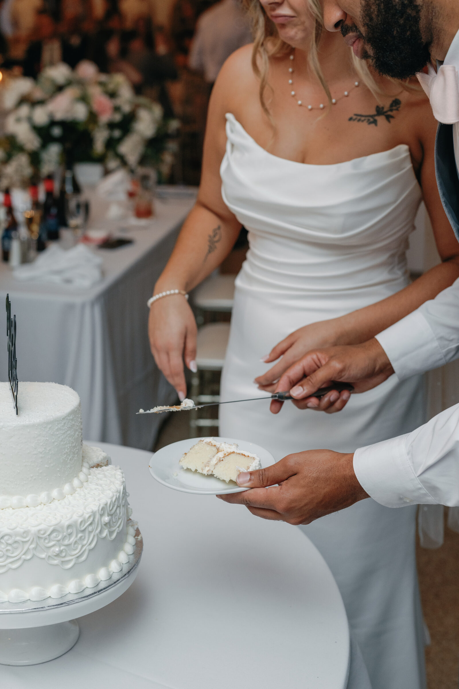 A close-up of the couple cutting and plating a slice of their white tiered wedding cake during the reception.