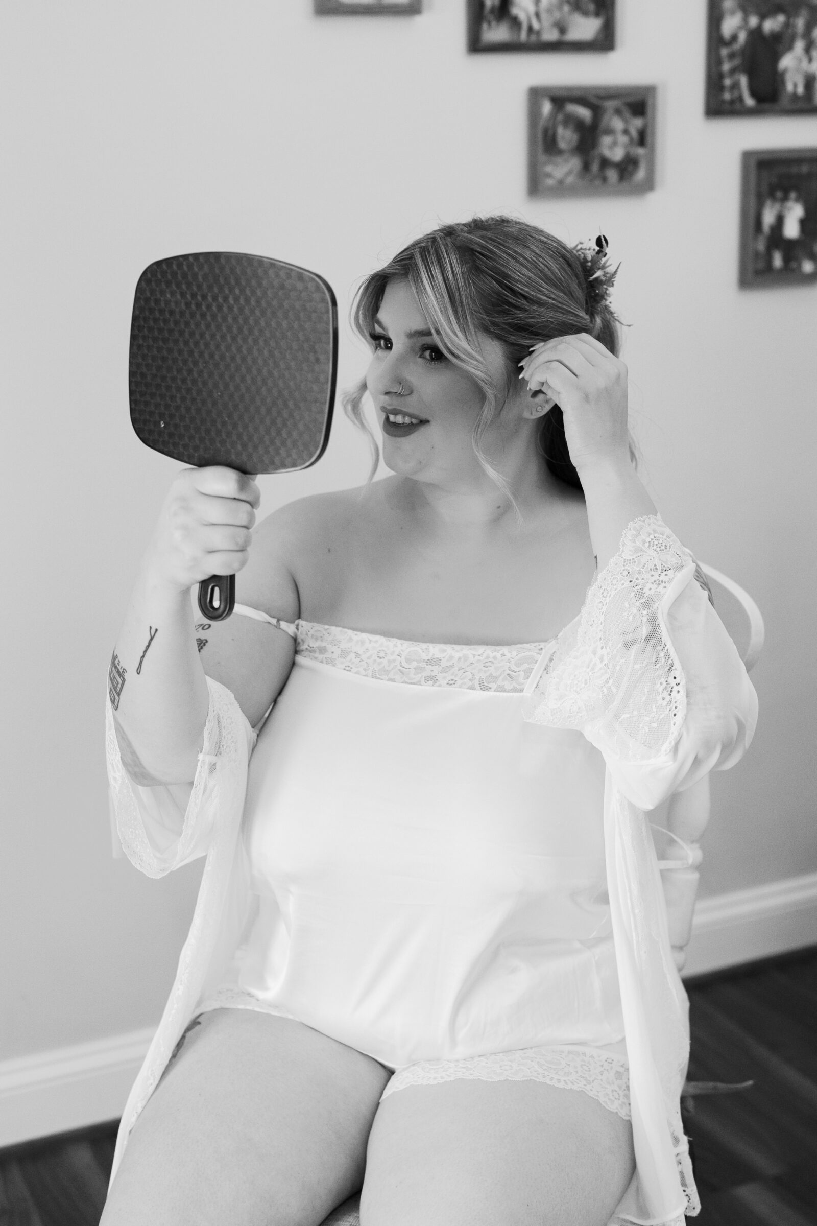 Bride getting ready on the wedding morning, adjusting her hair while looking into a handheld mirror, captured in soft black and white for an elegant, timeless feel.