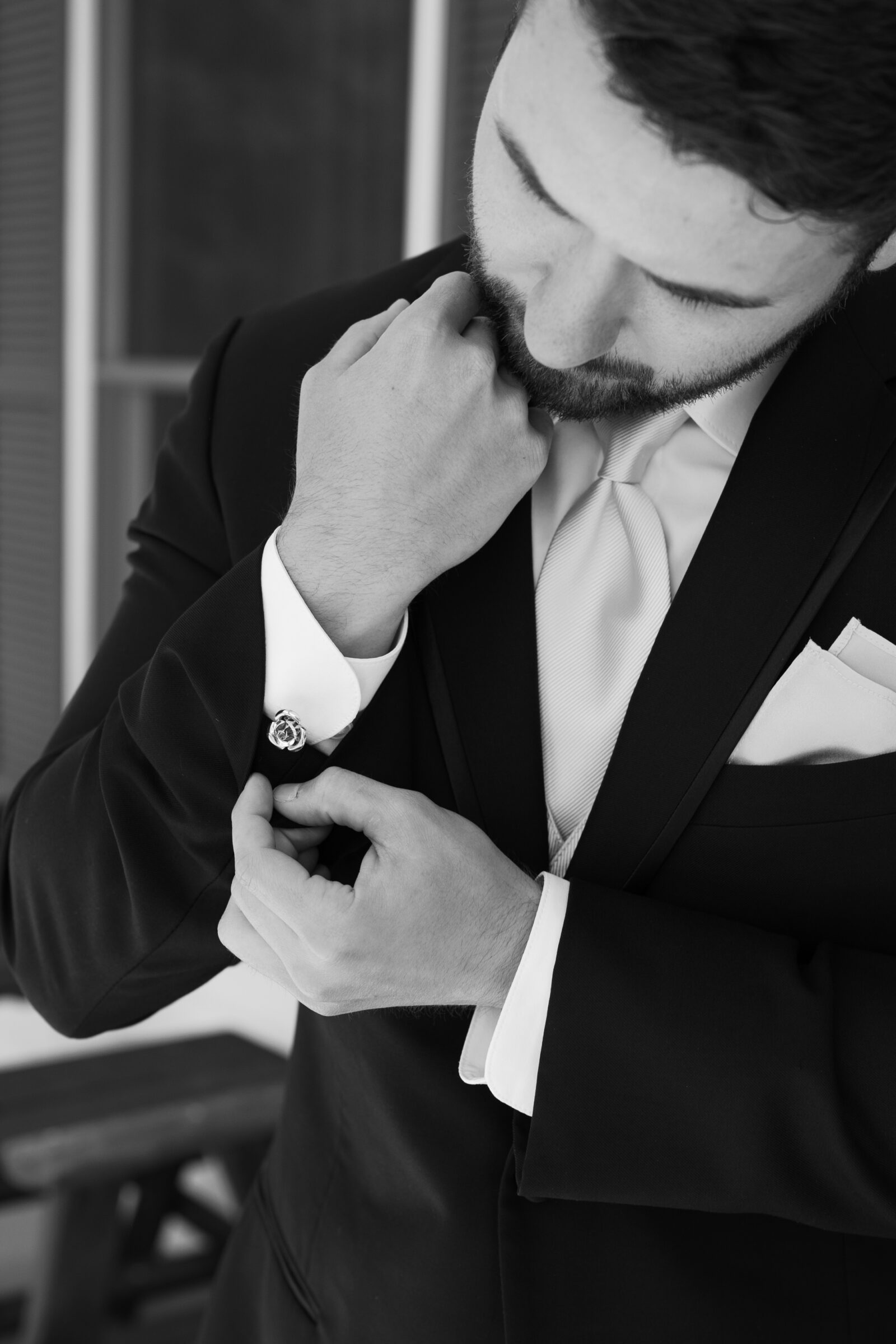 Southern MD Wedding Photographer | Close-up black and white portrait of the groom adjusting his cufflinks, highlighting the classic details of his suit and tie.