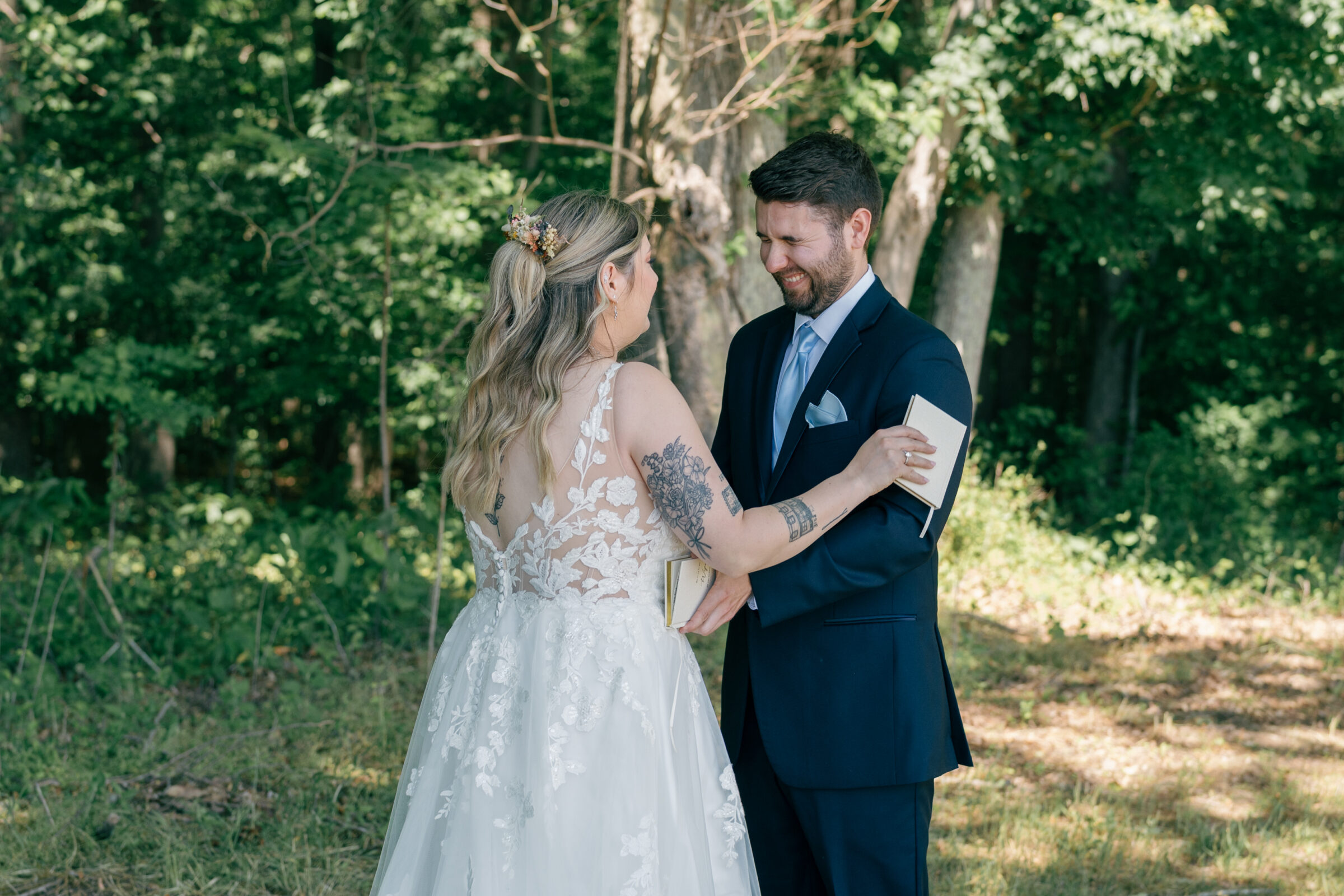 Bride and groom sharing a joyful moment during their private vow exchange in a wooded area on the wedding day.
