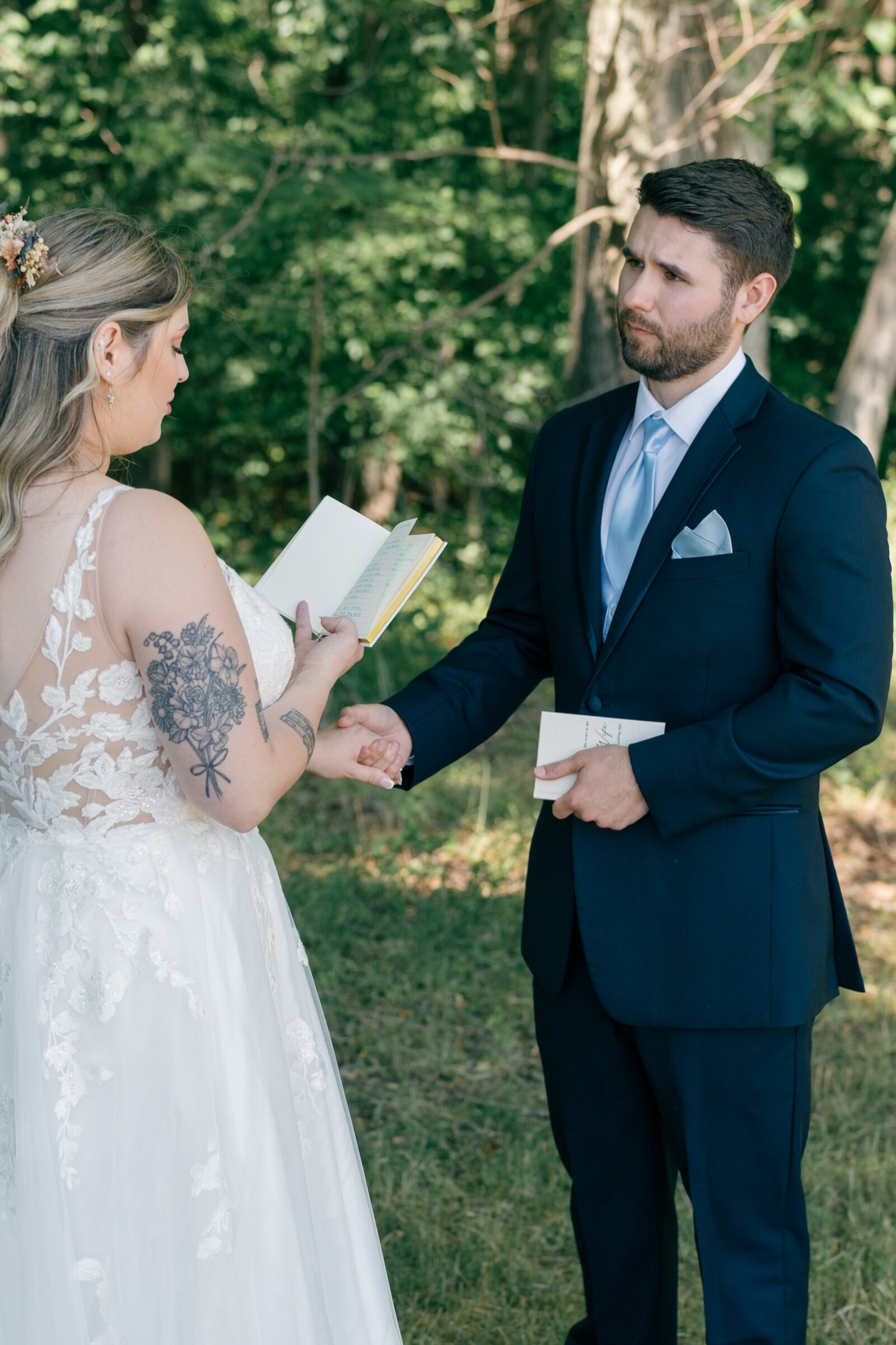 Bride and groom exchanging heartfelt vows in a wooded clearing during their Southern Maryland wedding, holding hands and reading from vow books.