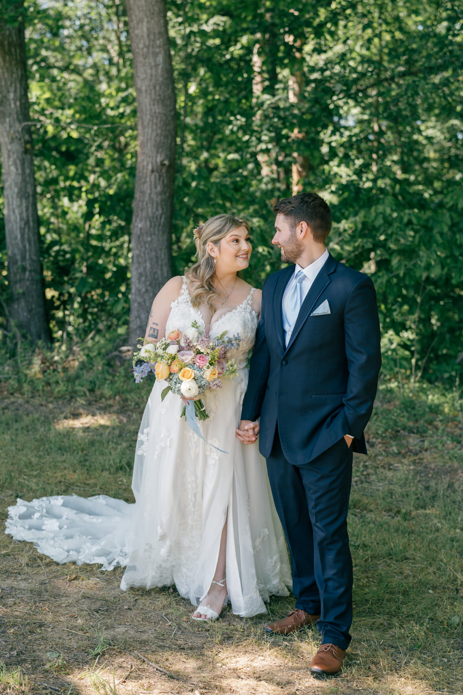 Southern MD Wedding Photographer | Bride and groom holding hands and smiling at each other in a wooded clearing, her wildflower bouquet adding soft spring colors.