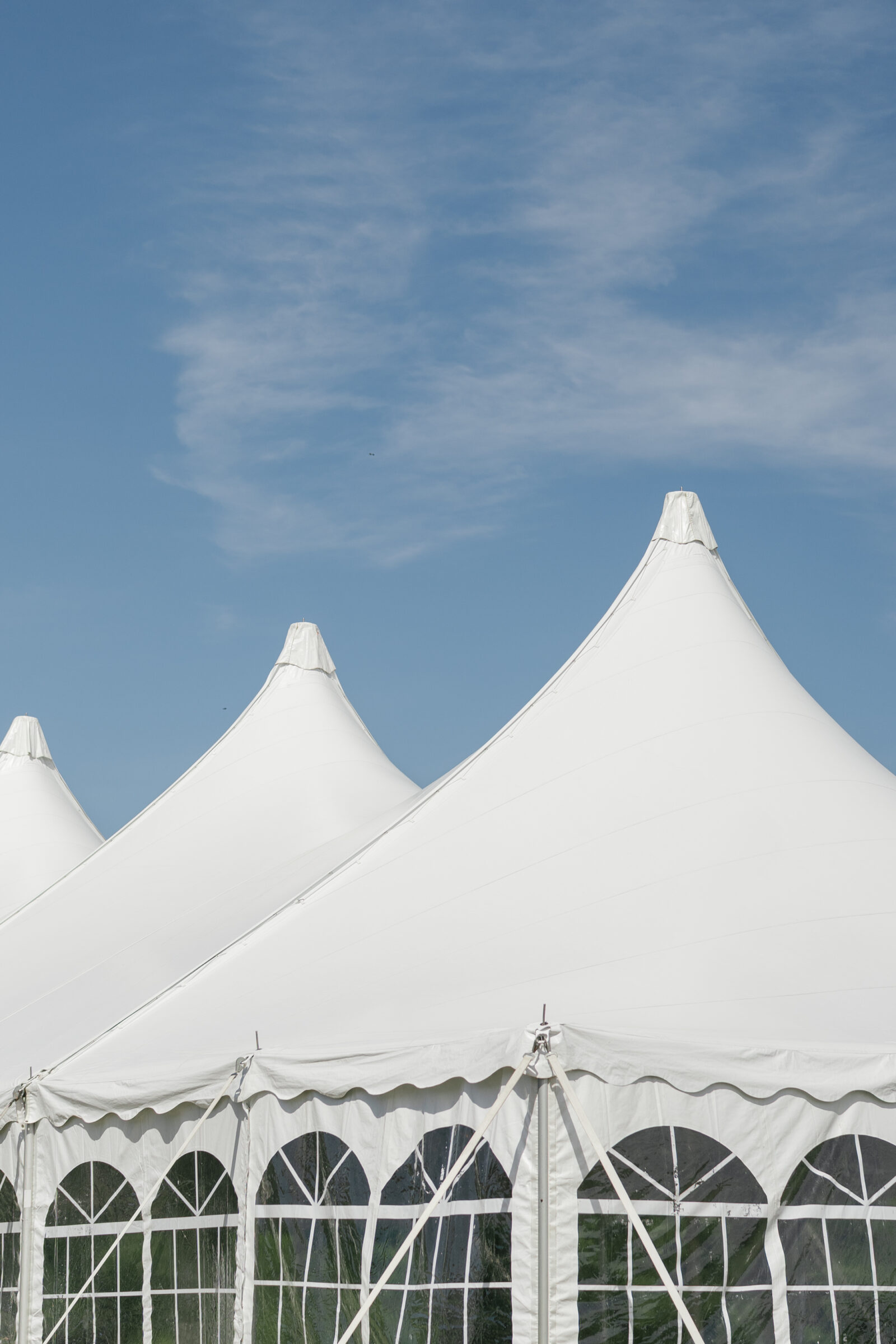 Peaked white wedding tent tops set against a bright blue sky, creating a classic and airy outdoor celebration backdrop.