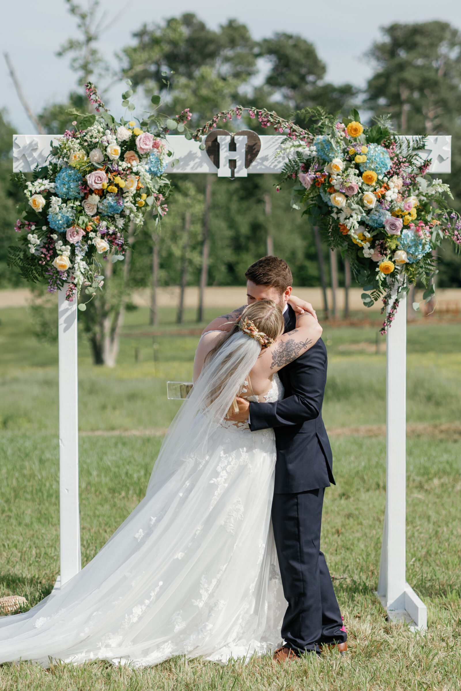 Southern Maryland Wedding Photographer | The bride and groom embrace under a floral-covered wooden arch moments after being pronounced married.
