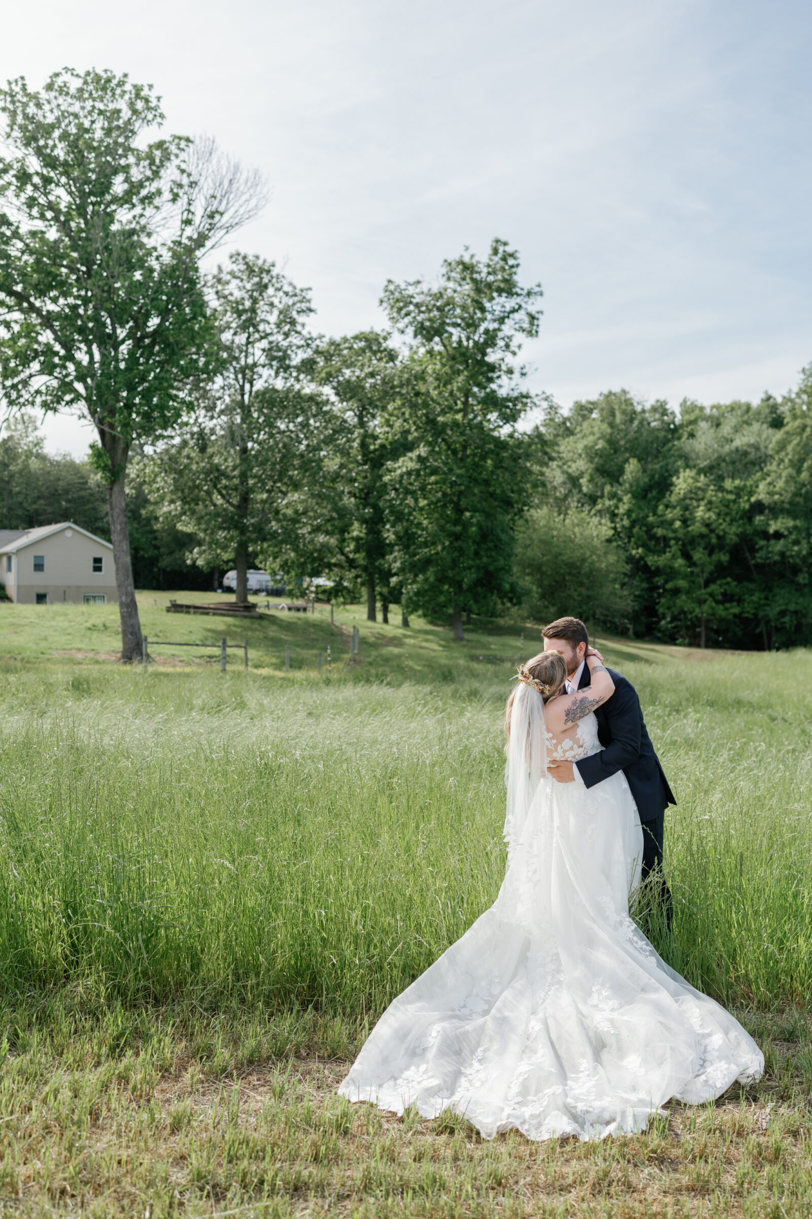 Southern Maryland Wedding Photographer | The bride and groom share a kiss in a wide open field, her lace train spread behind them in the grass.