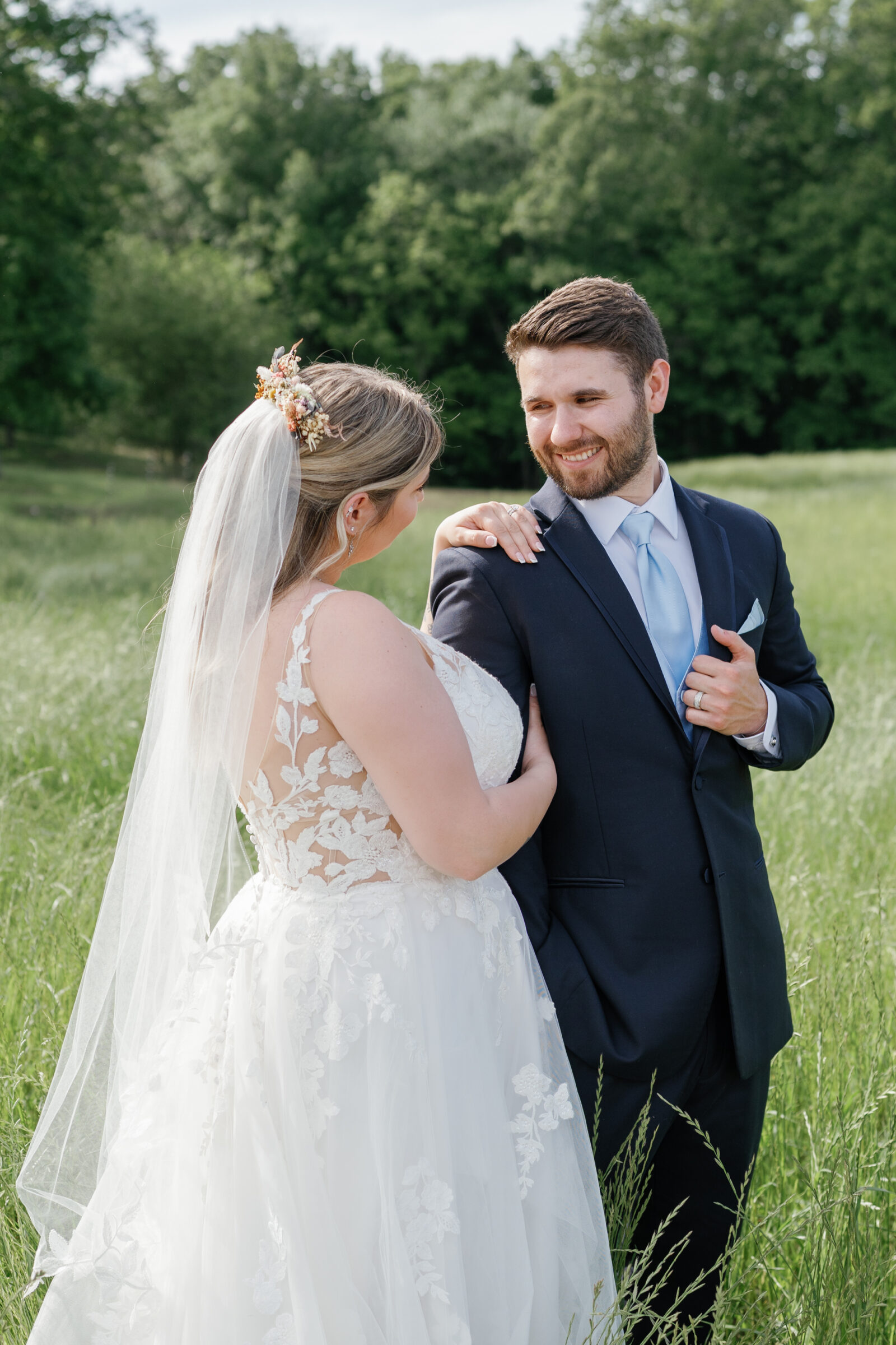 The bride rests her hand on the groom’s shoulder as they smile at each other in a grassy field in Southern Maryland.