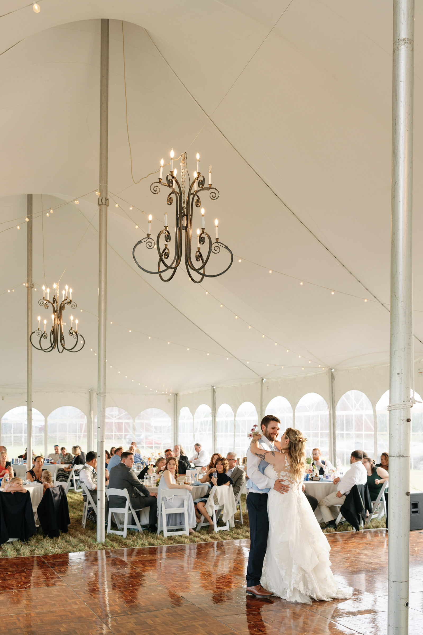 The bride and groom share their first dance under the tent, surrounded by guests and warm string lights.