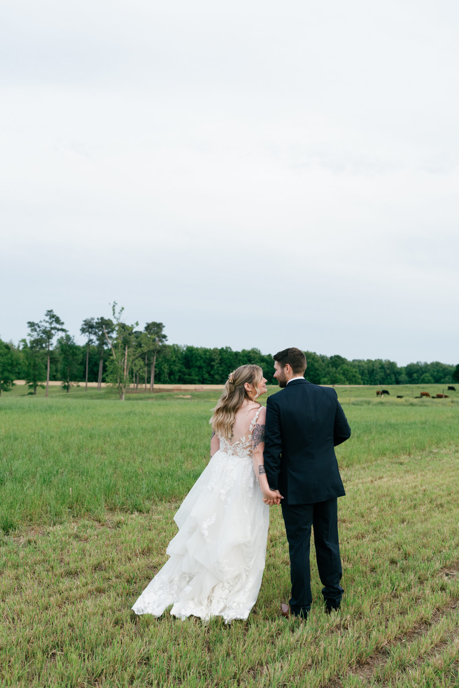 The bride and groom walk hand-in-hand through an open field, sharing a quiet moment after their ceremony.