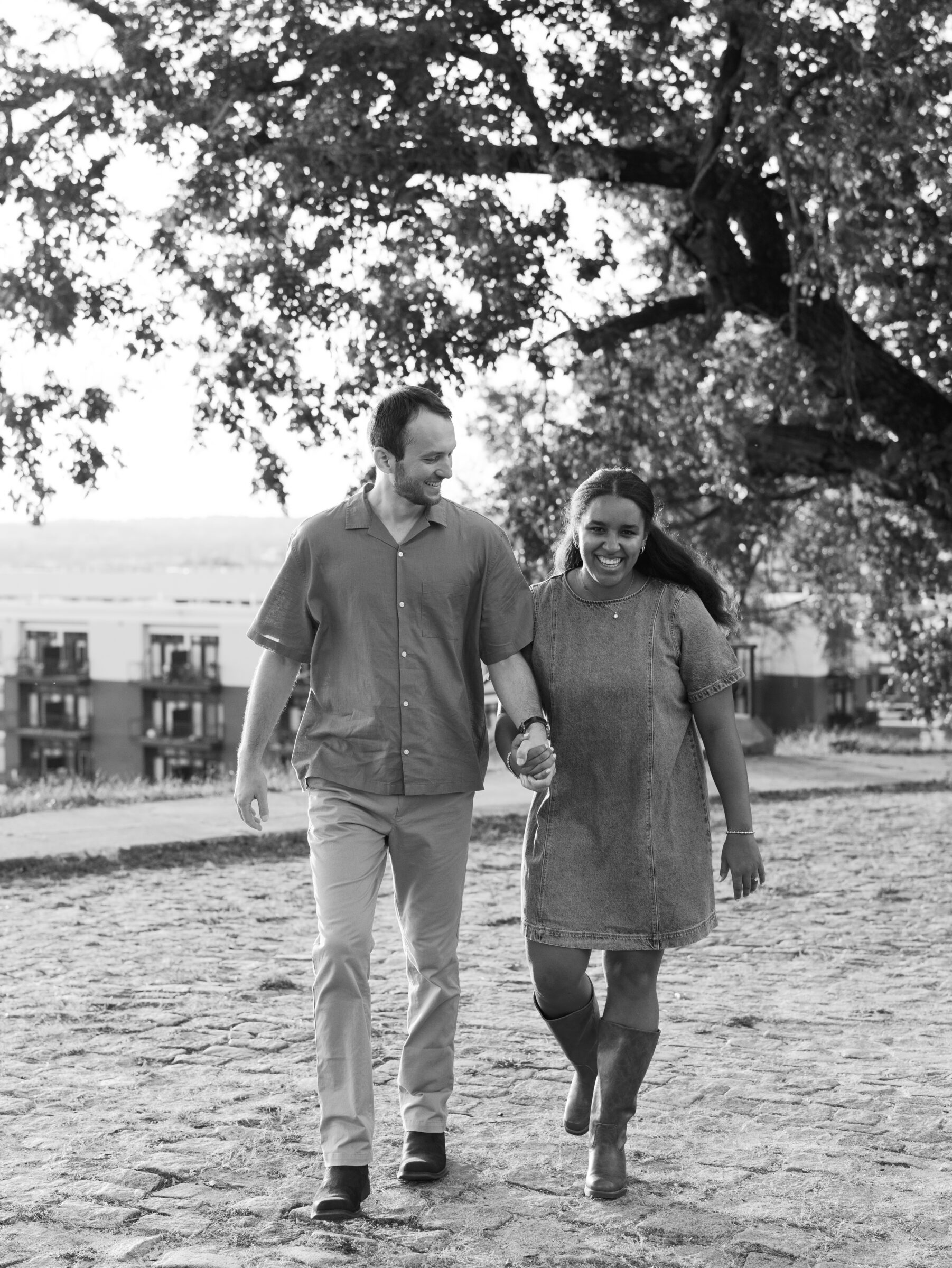 A couple walks hand in hand across the cobblestone path at Libby Hill Park during their Richmond engagement session, smiling together in a candid black-and-white moment.
