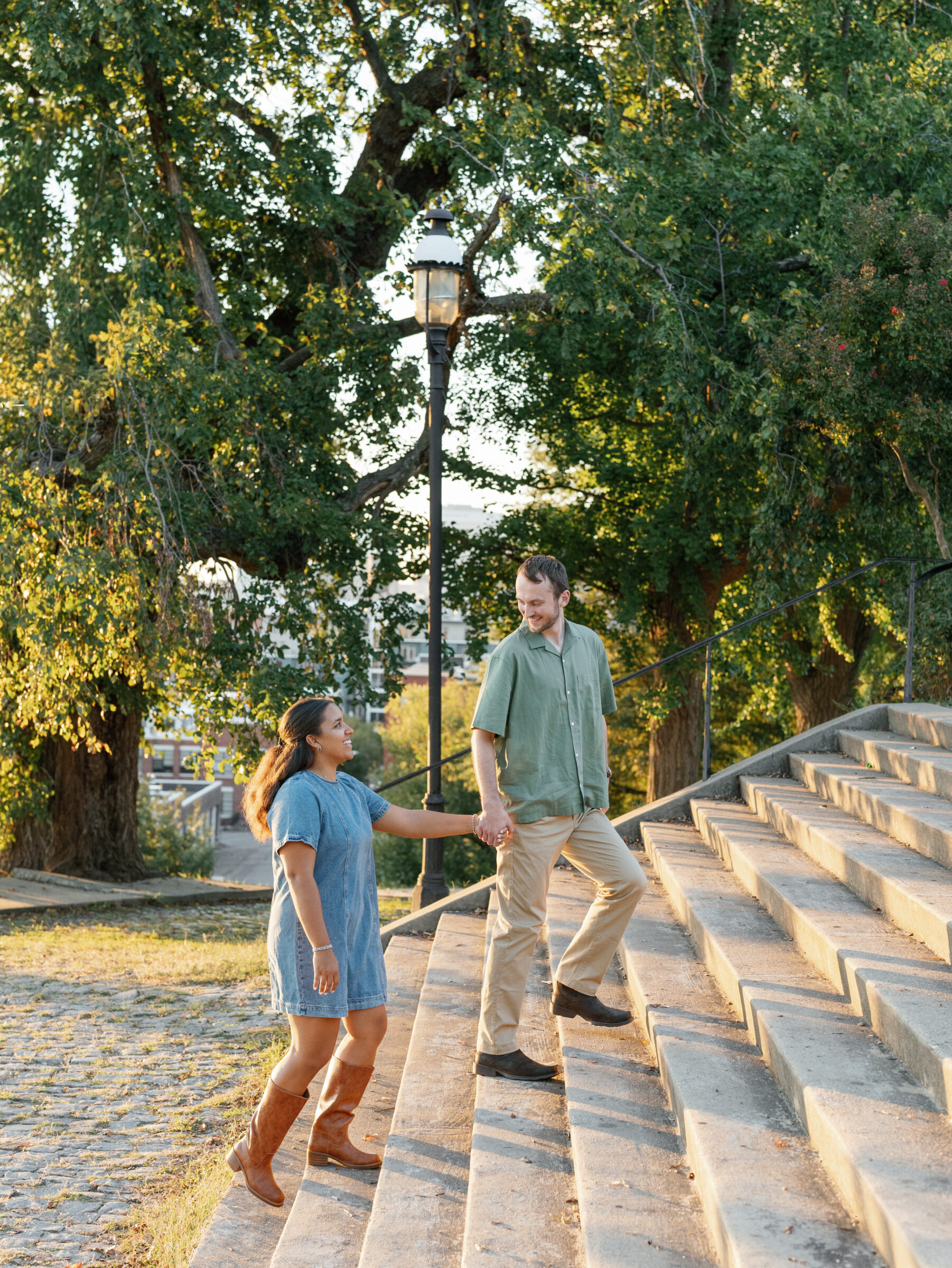 A couple walks hand in hand up the stone steps at Libby Hill Park during their Richmond engagement session, surrounded by golden light and lush trees.