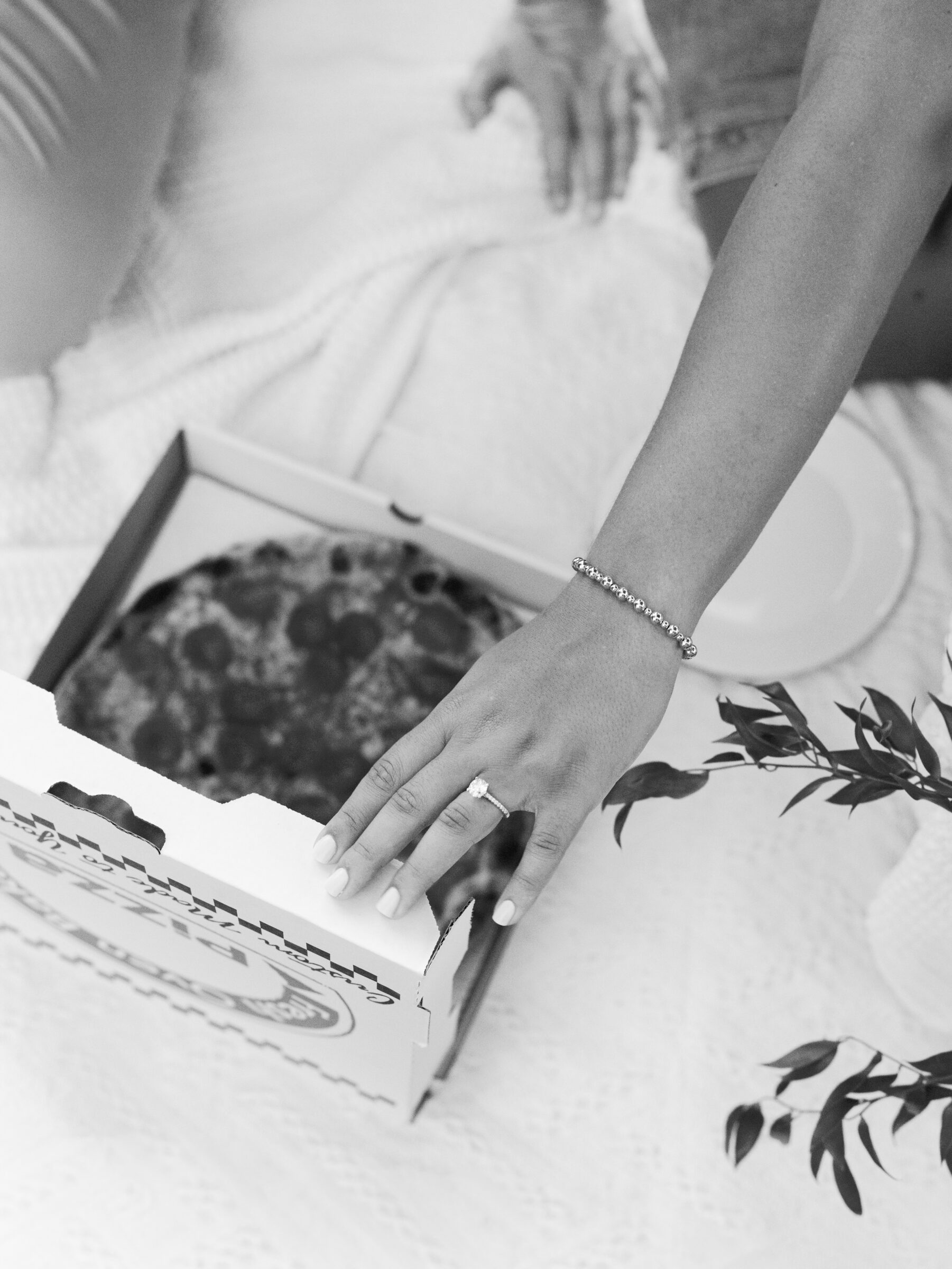 A close-up of the bride-to-be opening a pizza box during the picnic at Libby Hill Park, her engagement ring catching the light as she lifts the lid.