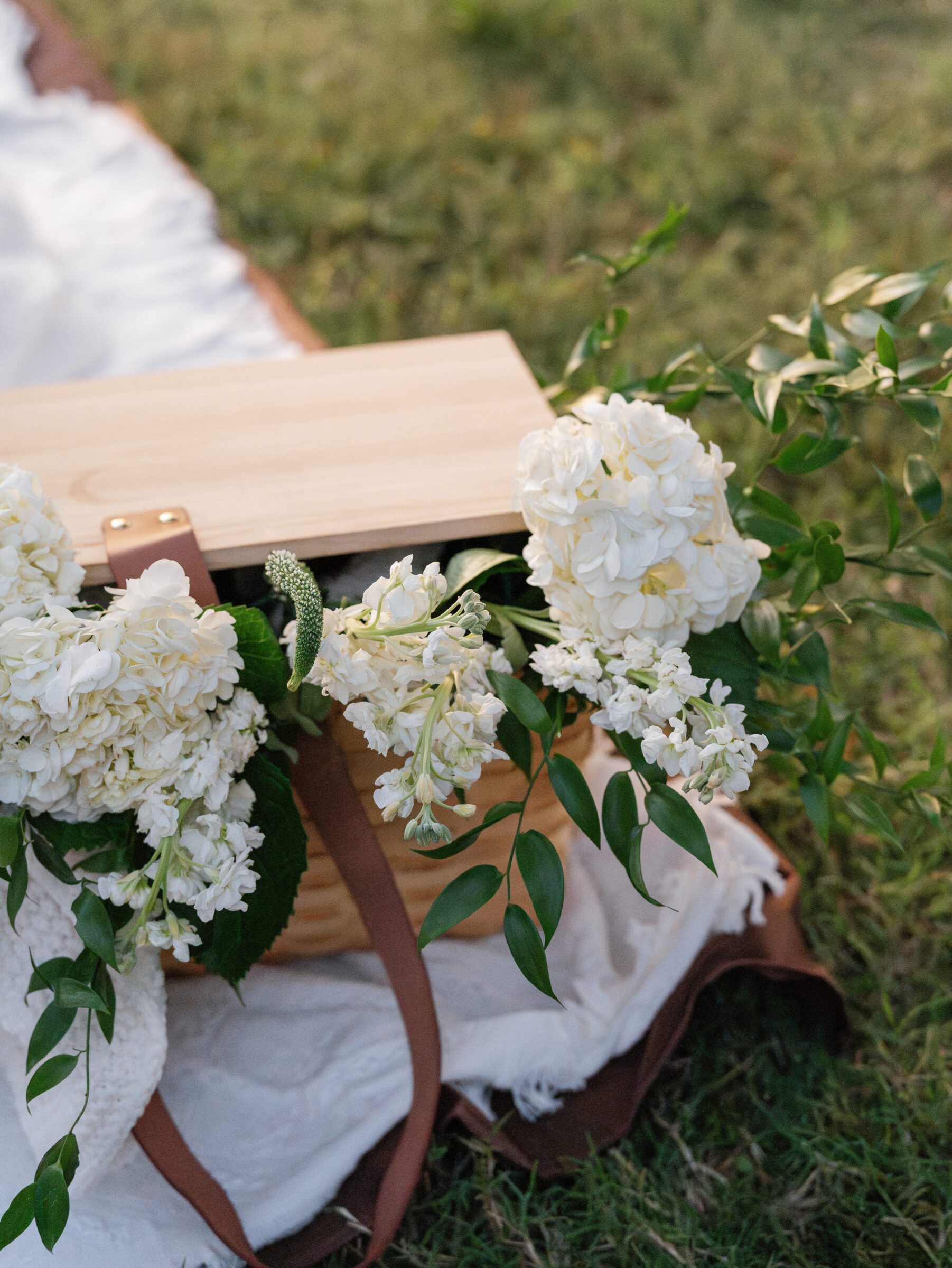 A close-up of a woven picnic basket filled with white flowers resting on a blanket during an engagement session at Libby Hill Park.