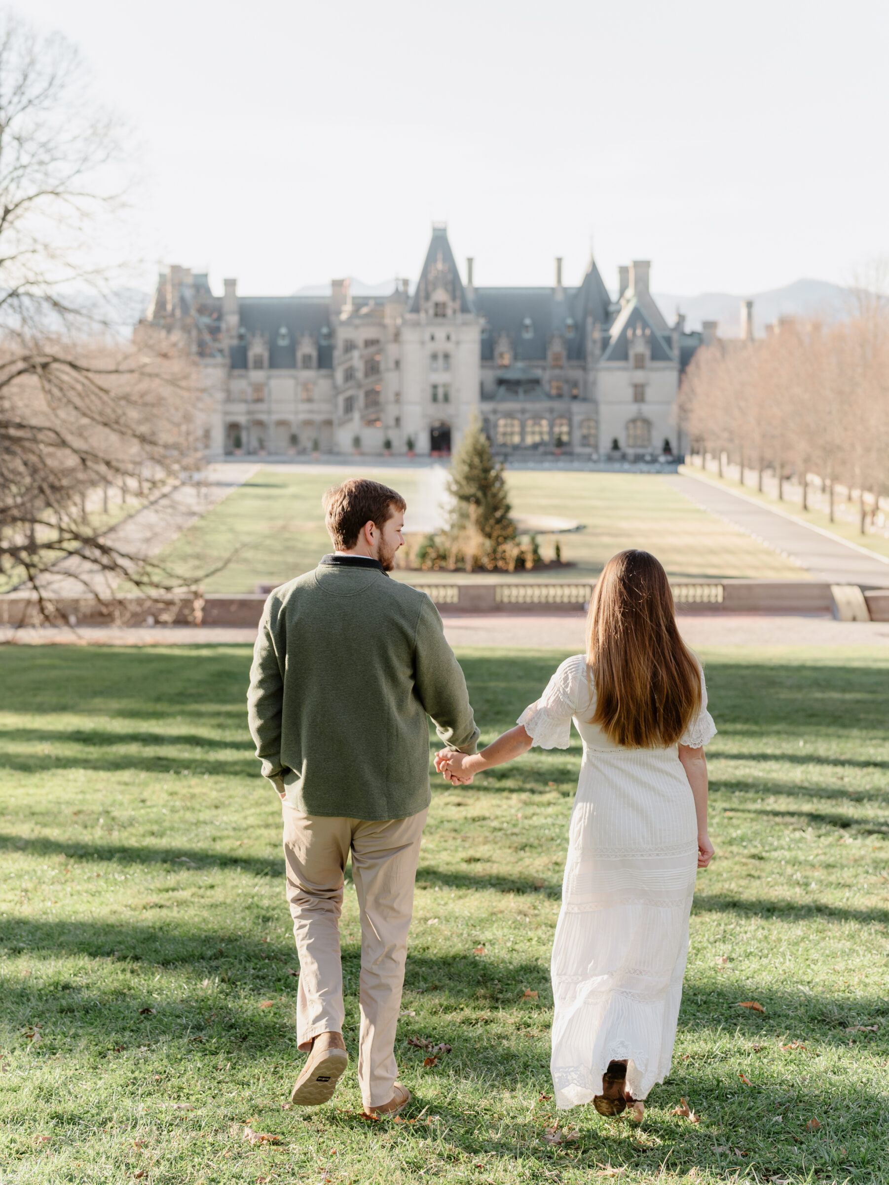 Couple walking hand in hand toward the Biltmore Estate during a fall engagement session in Asheville NC