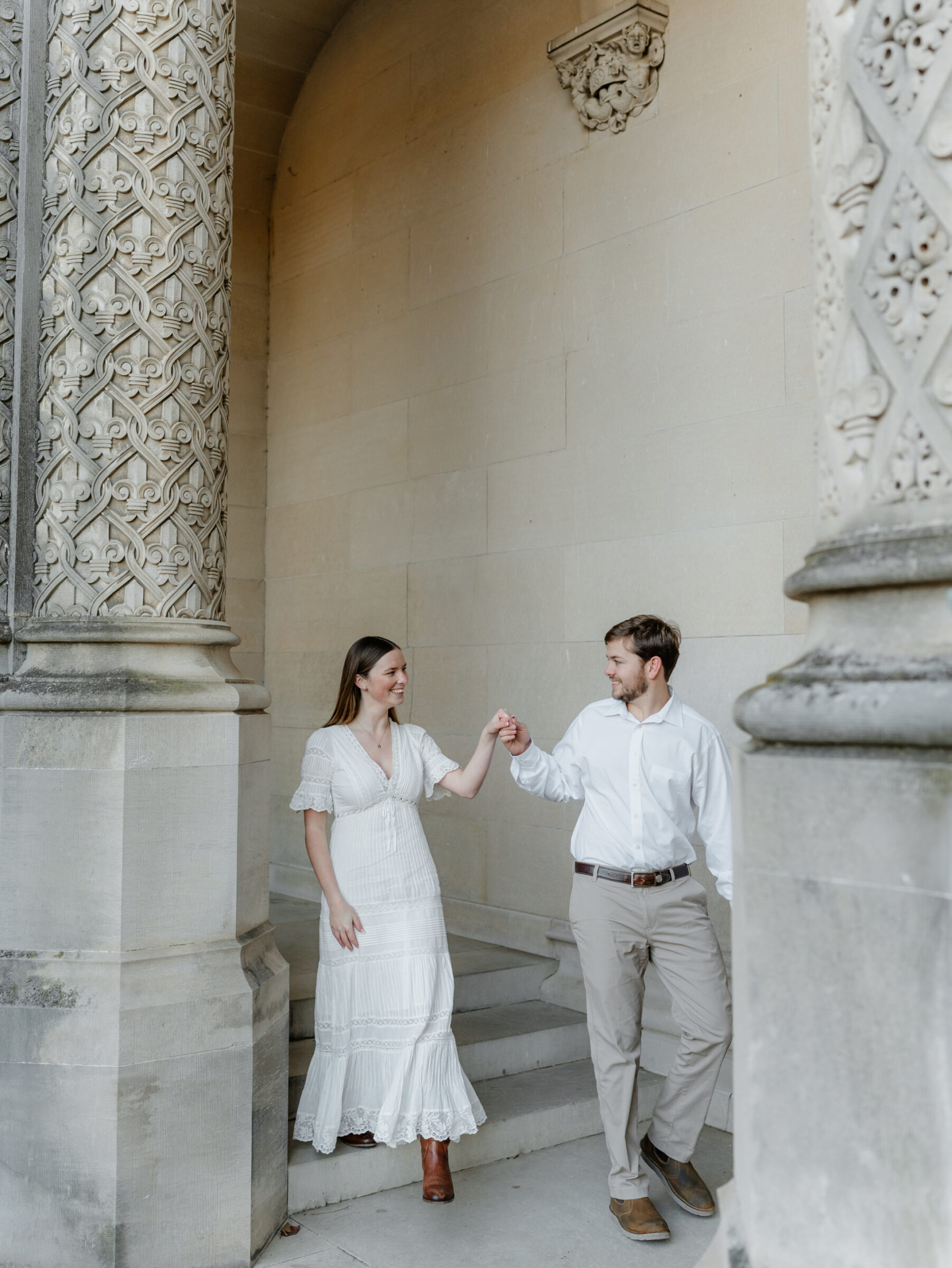 Couple holding hands beneath ornate stone columns during a fall engagement session at the Biltmore Estate in Asheville NC
